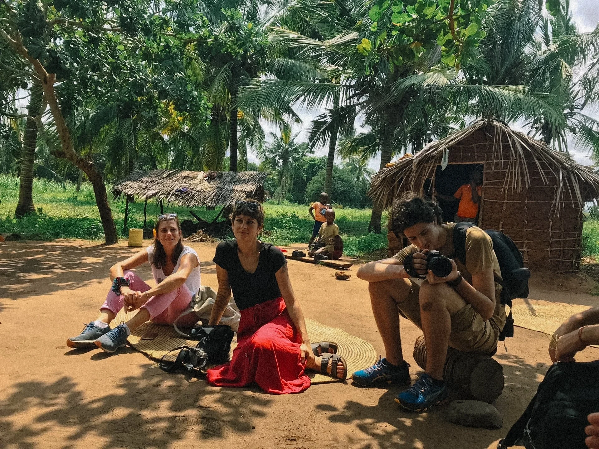 Group of people in a rural setting with palm trees and huts