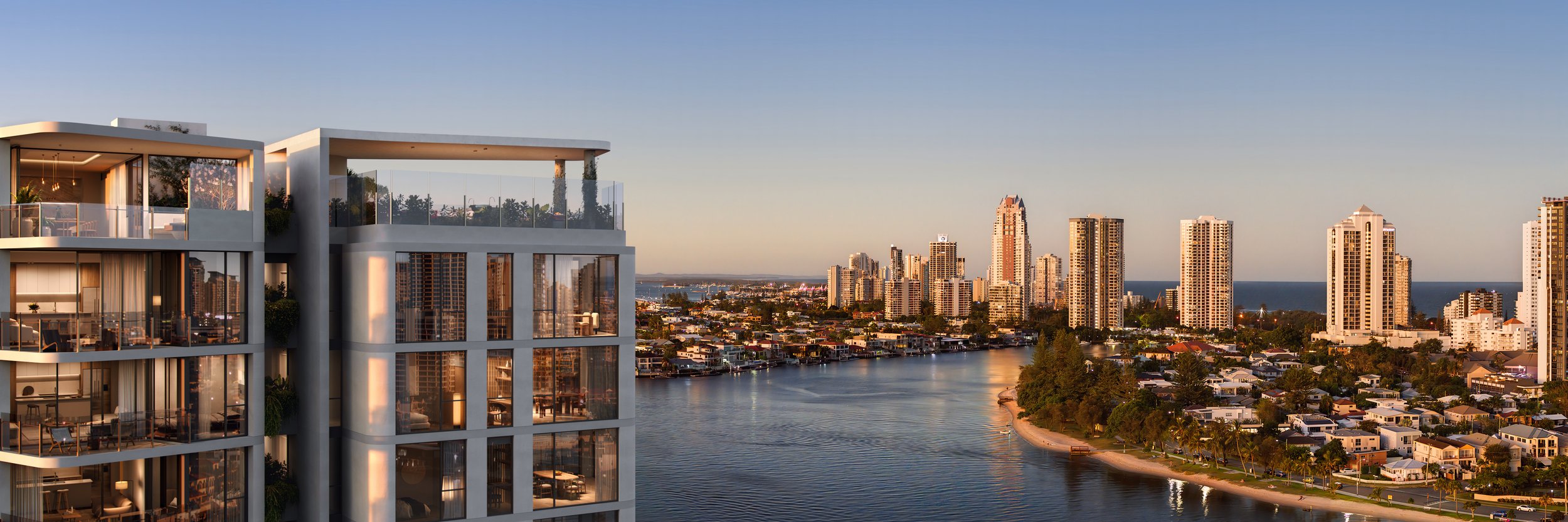 Modern apartment building with glass balconies overlooking river, city skyline in the background, and clear sky at sunset.