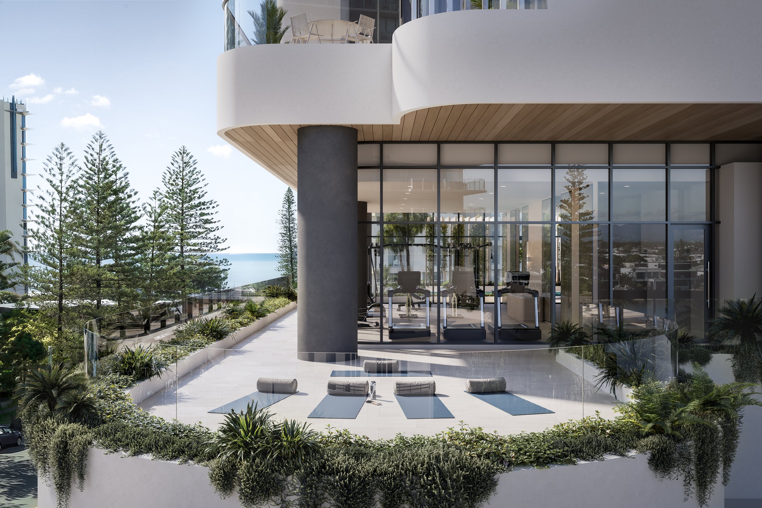 Modern building with glass windows and a terrace featuring yoga mats and plants, overlooking trees and the ocean.