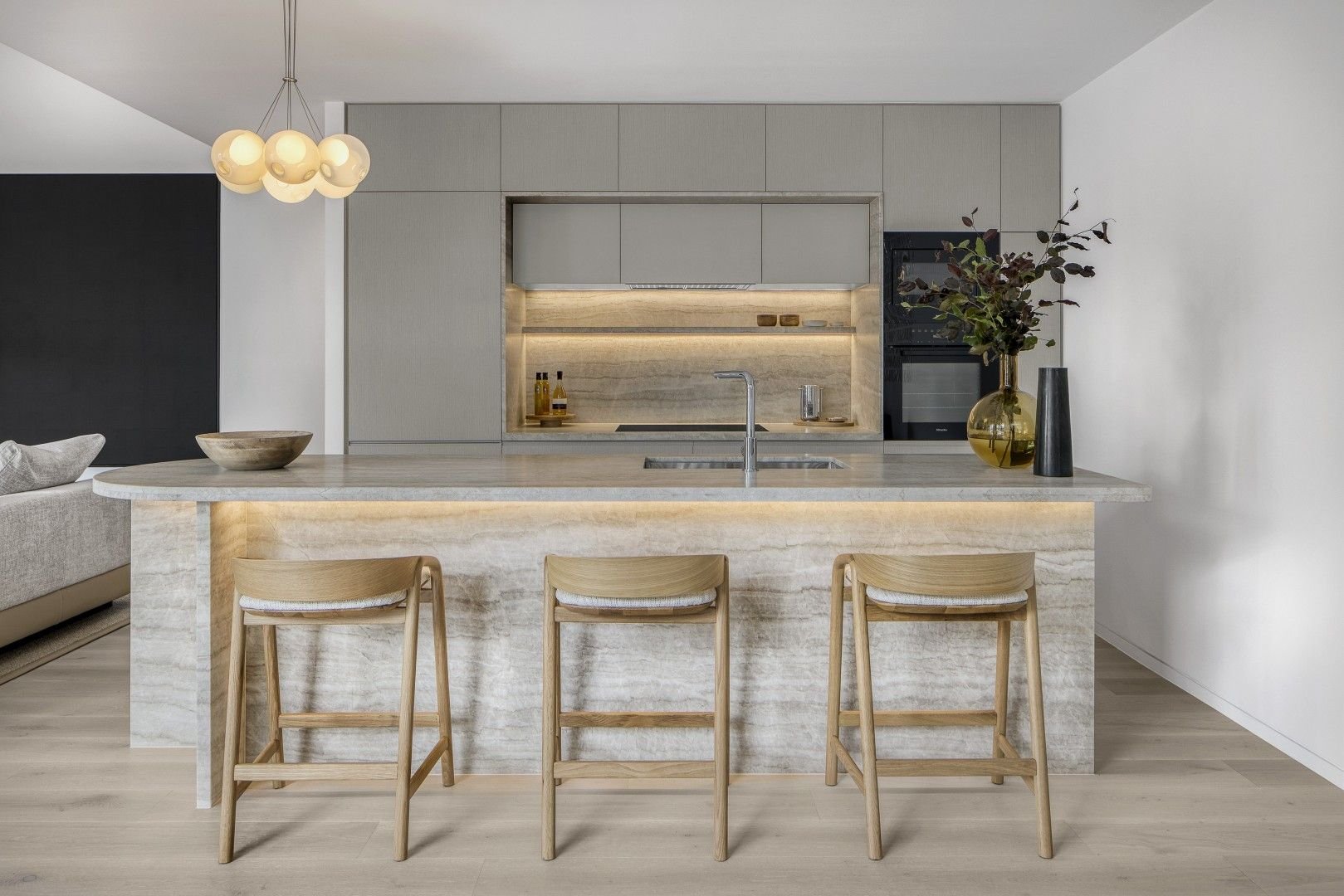Modern kitchen with island, wooden stools, pendant light, and vase with greenery on the counter.