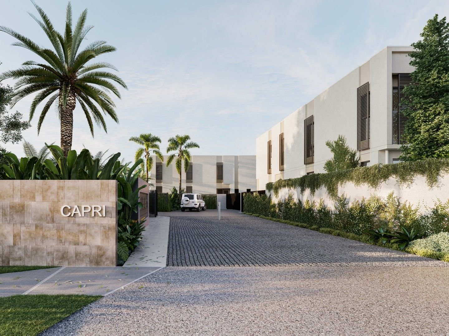 Modern building entrance with "Capri" sign, tall palm trees, lush greenery, gravel driveway, and a white vehicle parked.