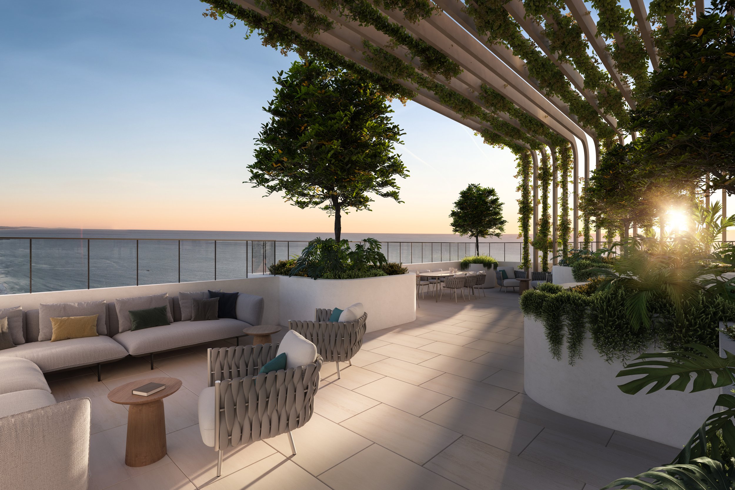 Modern rooftop terrace with comfortable seating, potted trees, and plants, offers ocean view at sunset.