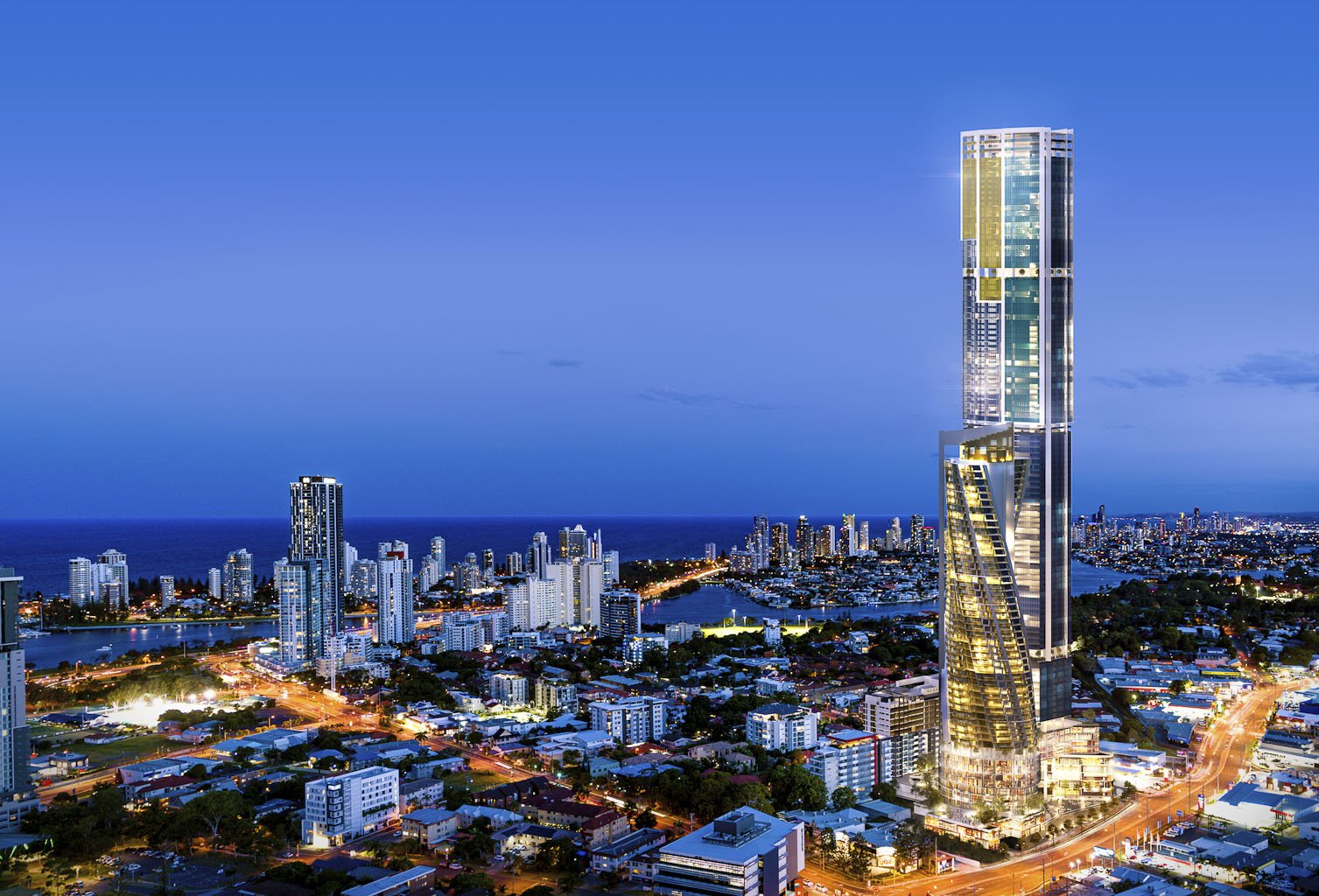 Cityscape with tall modern skyscraper and surrounding buildings at dusk, ocean in the background.