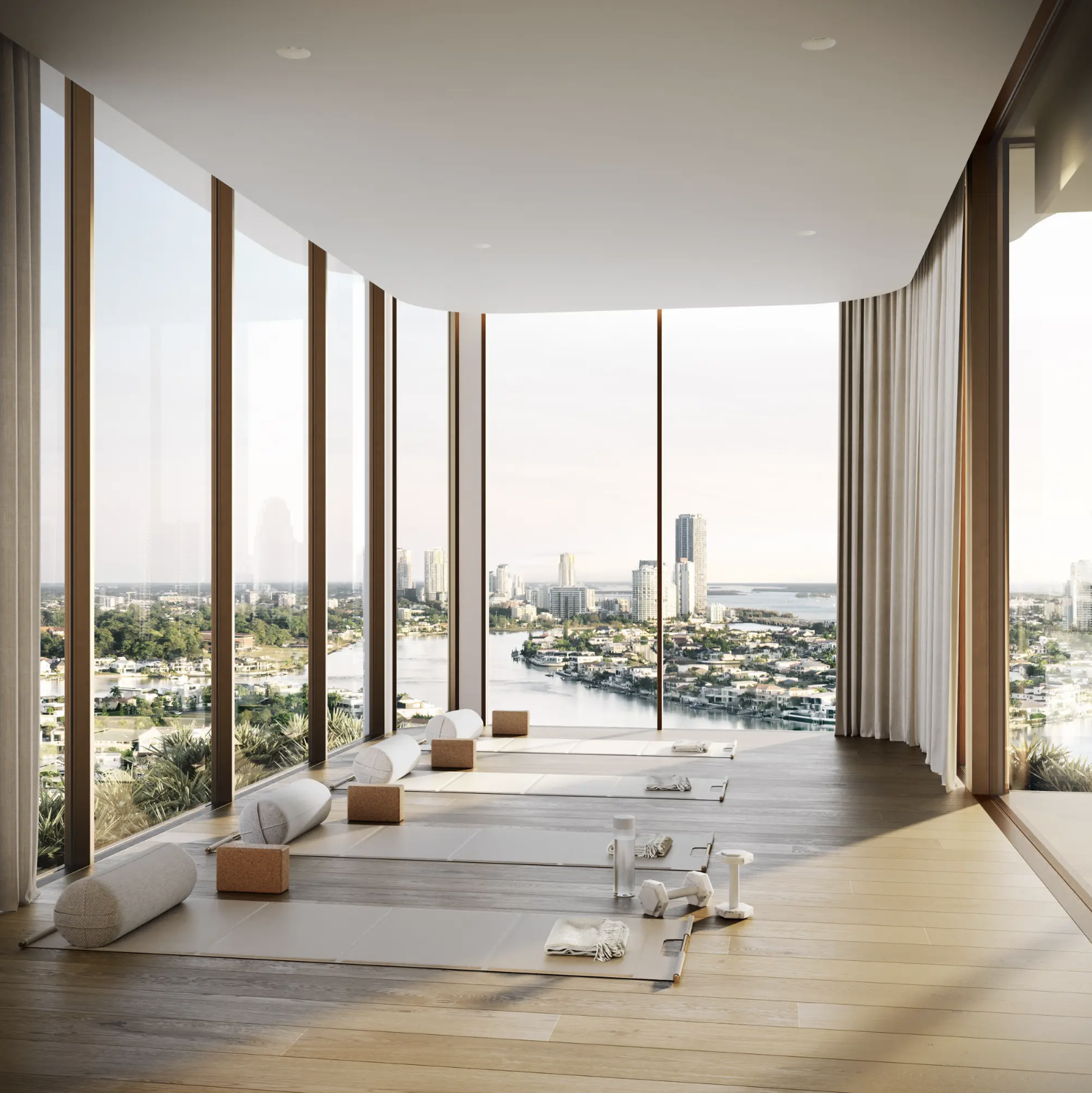 Bright yoga studio with large windows, overlooking a cityscape and waterway, featuring yoga mats and props arranged on a wooden floor.