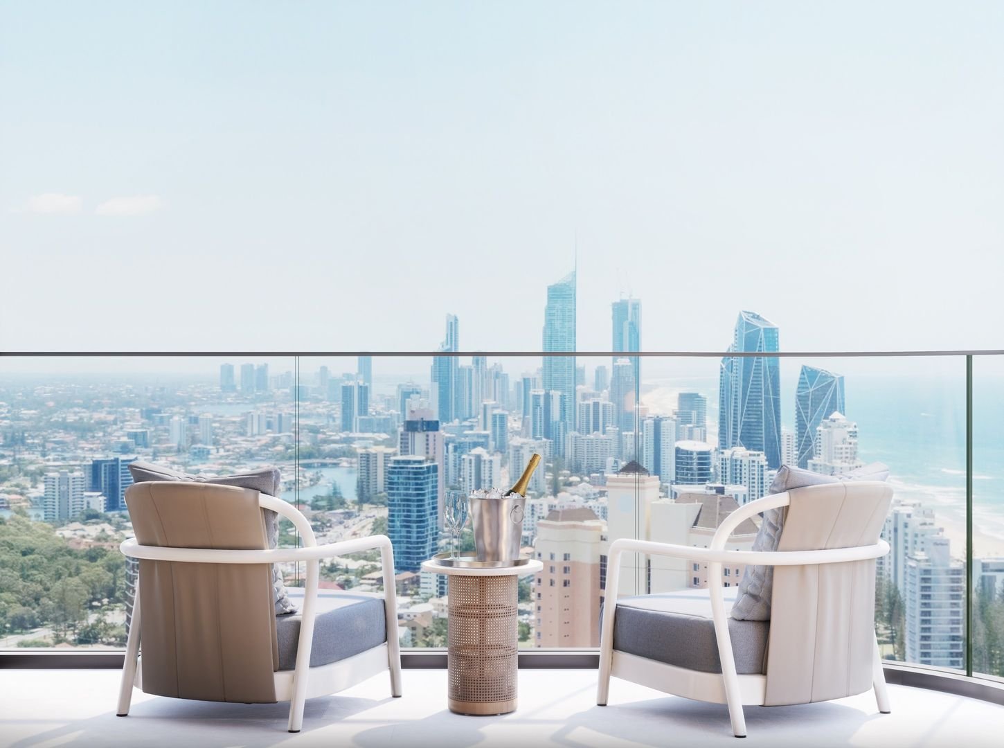 Modern balcony with two armchairs and a table, overlooking city skyscrapers and ocean view.