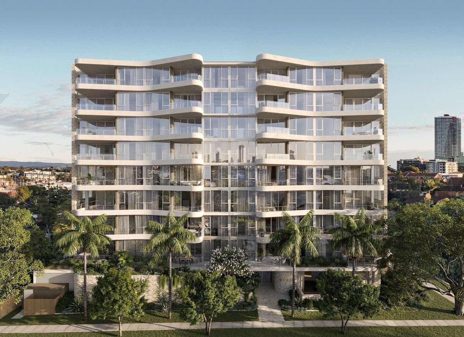 Modern apartment building with glass balconies, surrounded by palm trees and greenery, cityscape in background.