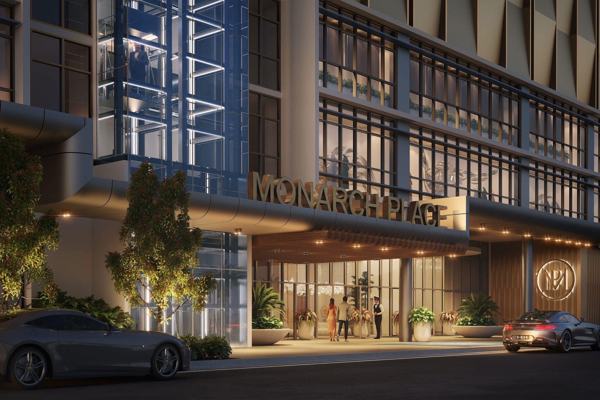 Exterior view of Monarch Place entrance with illuminated signage, modern architecture, glass elevator, people at entrance, and parked luxury cars.