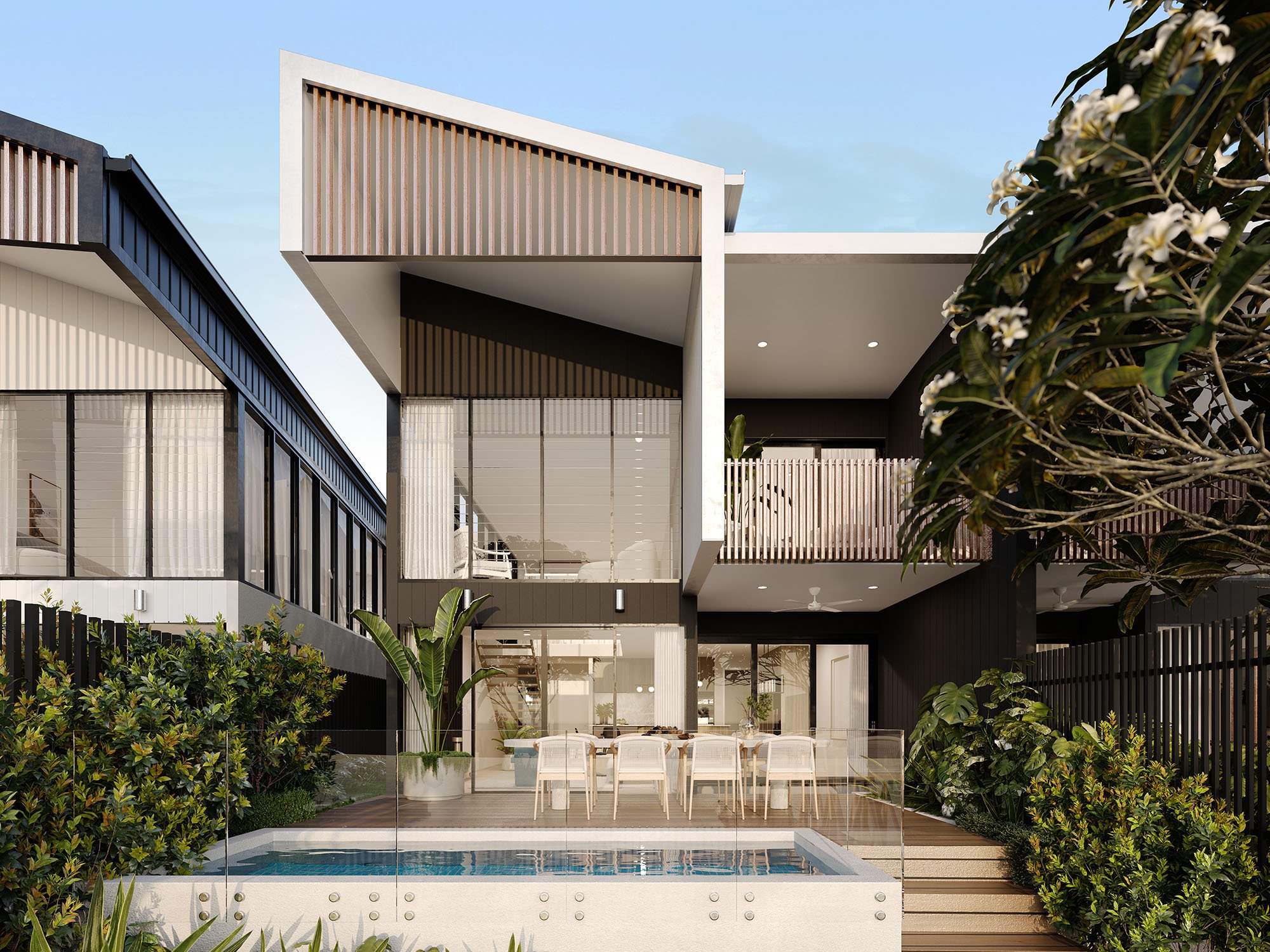 Modern two-story house exterior with large windows, overhanging roof, and outdoor dining area beside a swimming pool; surrounded by lush greenery and flowering trees.