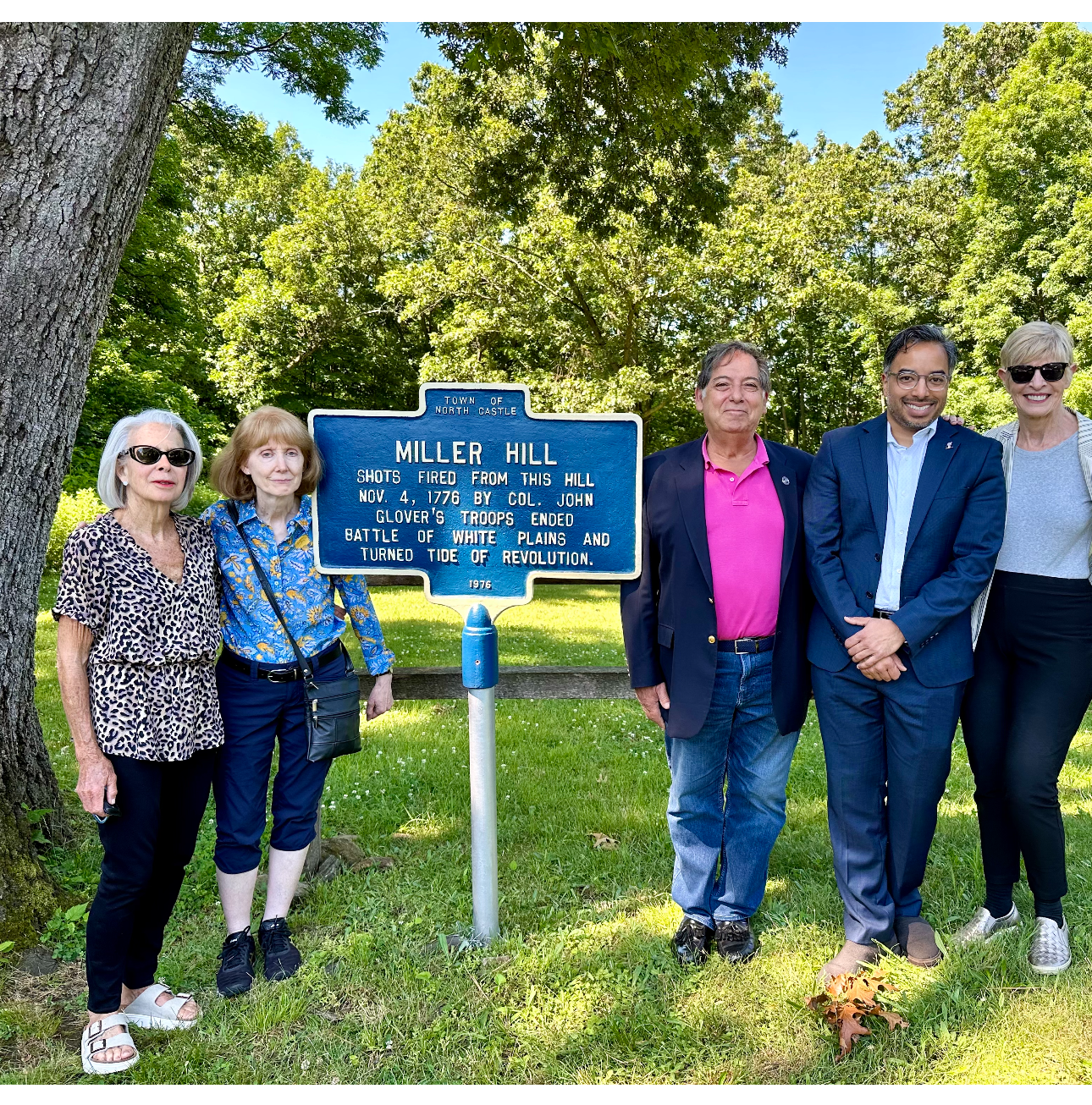 Five people standing in front of the Miller Hill historical marker, which details its significance in the American Revolutionary War, surrounded by lush green trees.