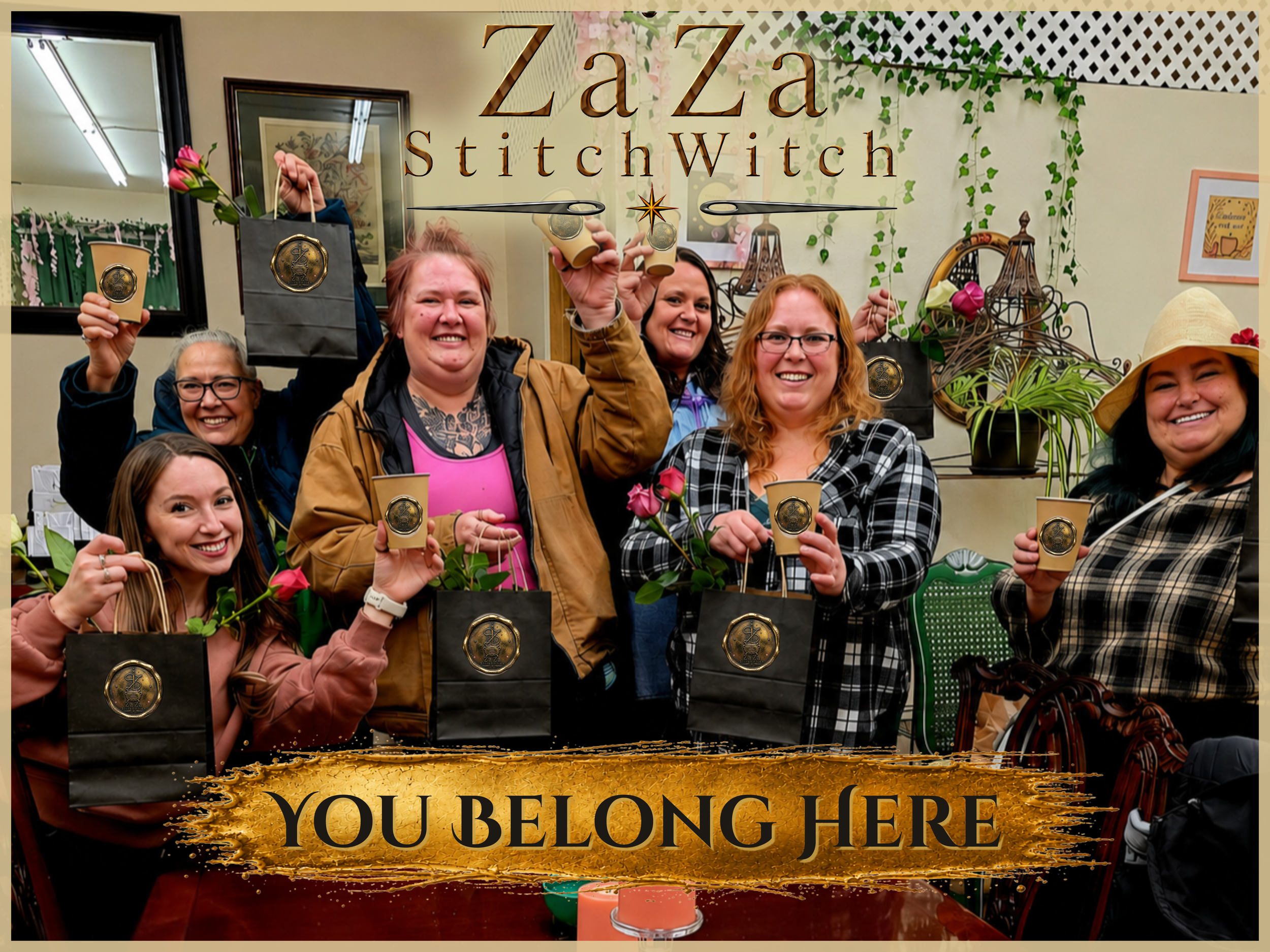 A group of women smiling and holding small cups of beverages, standing behind a sign that says, 'Zza Za StitchWitch You Belong Here,' with festive decorations and plants in the background.