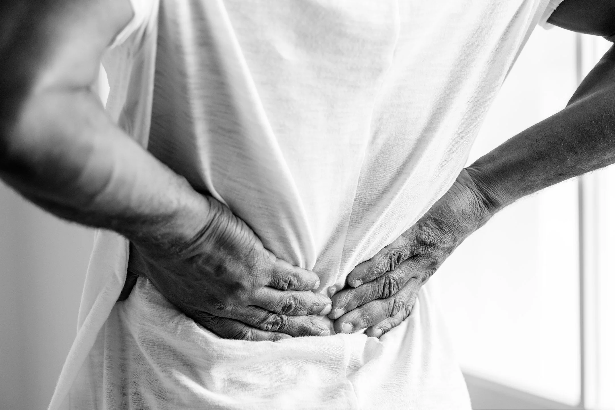 A person holding their lower back, a common reason people seek a chiropractor in Hastings.