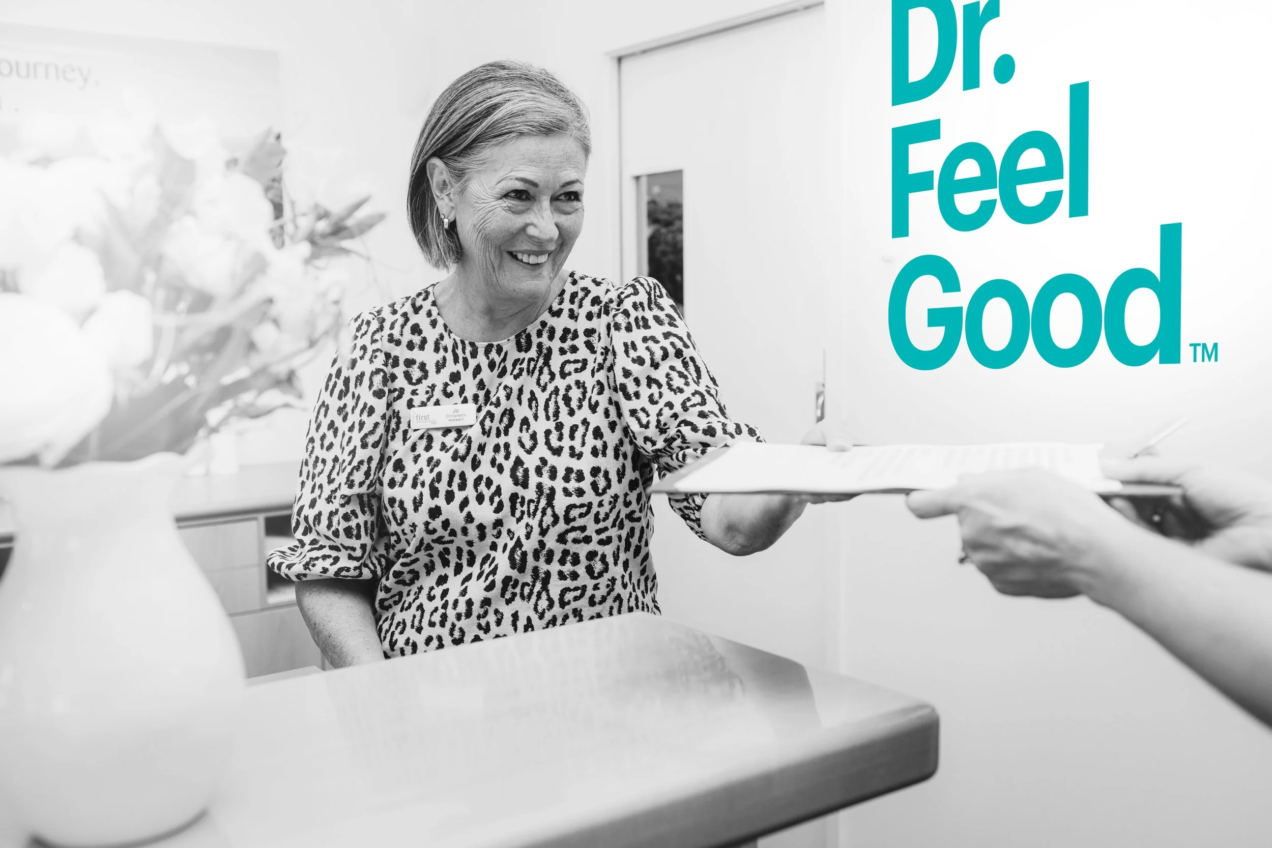 A patient smiles in an office with a "Dr. Feel Good" sign, representing a positive chiropractic experience in Hawke's Bay.