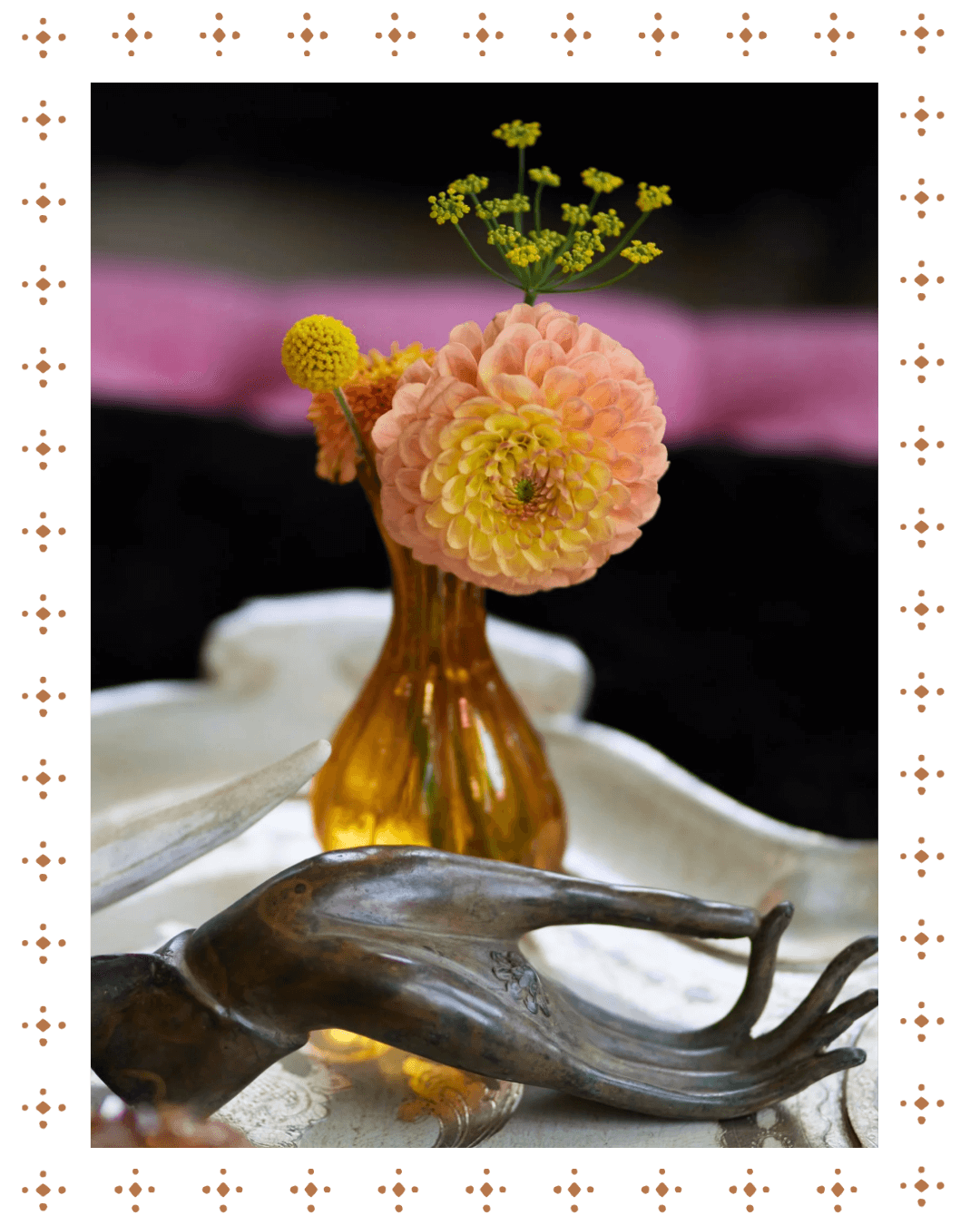 A small amber glass vase holding pink and yellow flowers, placed on a decorative surface with a black background.