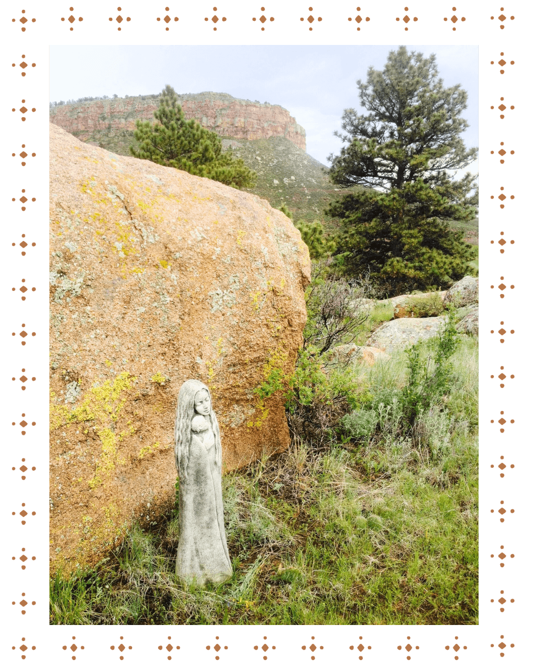 A small stone statue of a girl standing outdoors near a large rock with a mountain and trees in the background.