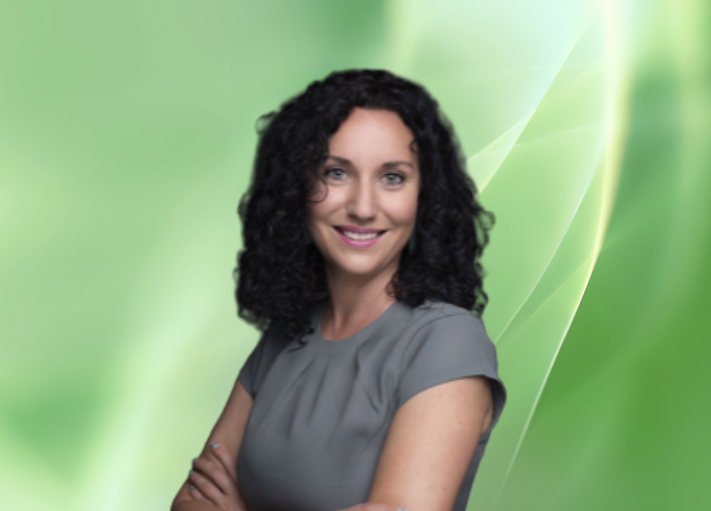 A woman with curly black hair and a gray dress standing against a green abstract background.