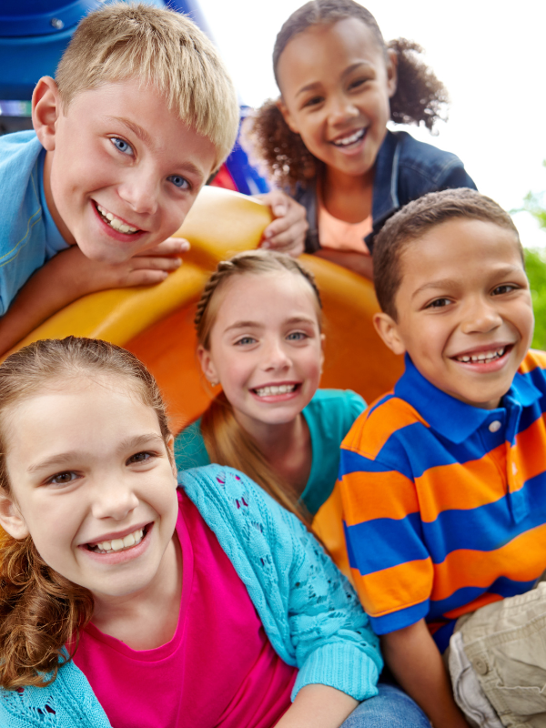 Group of five children smiling outdoors near a yellow structure, playing and having fun.