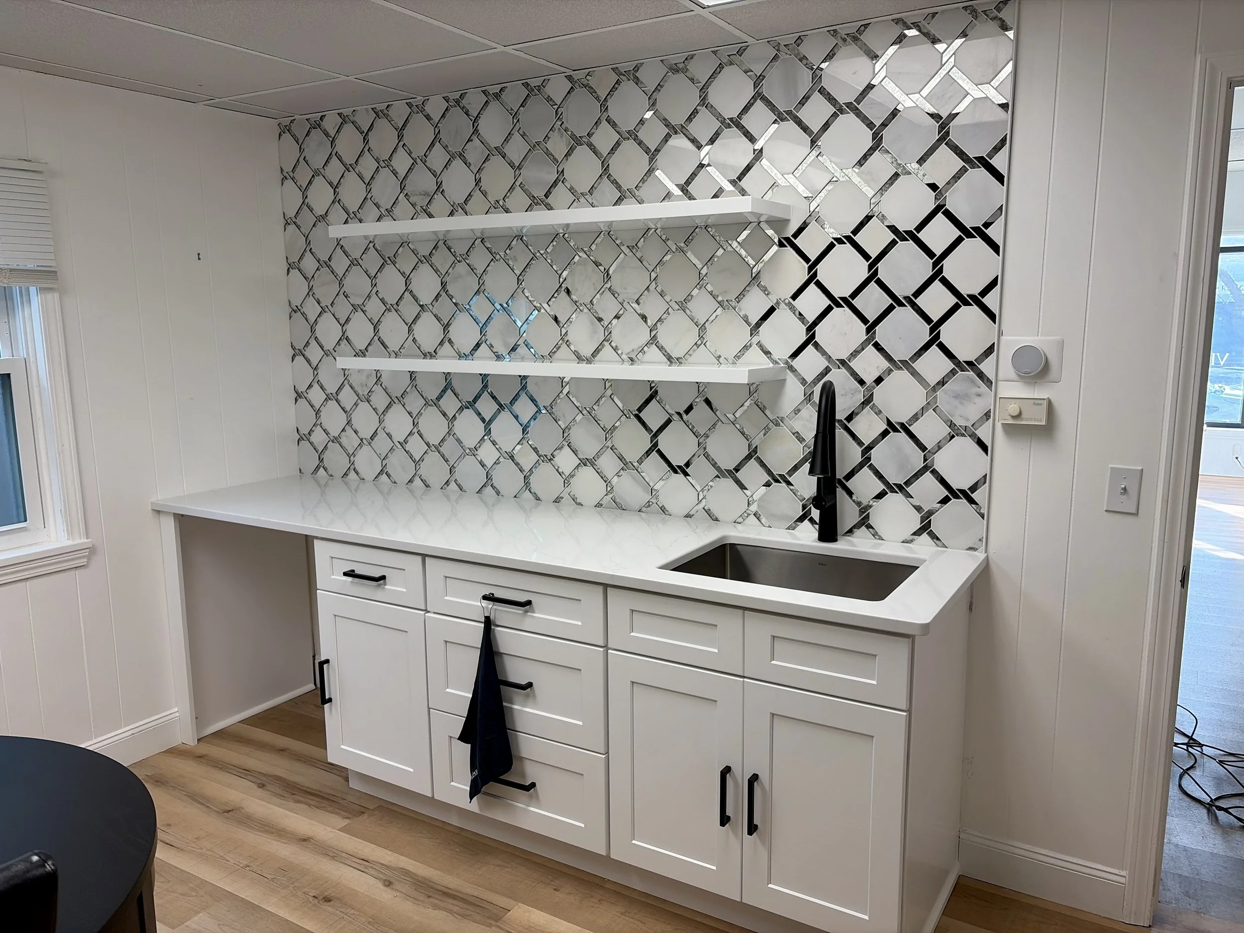 Kitchen with white cabinets, black handle pulls, black faucet, marble countertop, patterned tile backsplash, black sink, and open shelves.