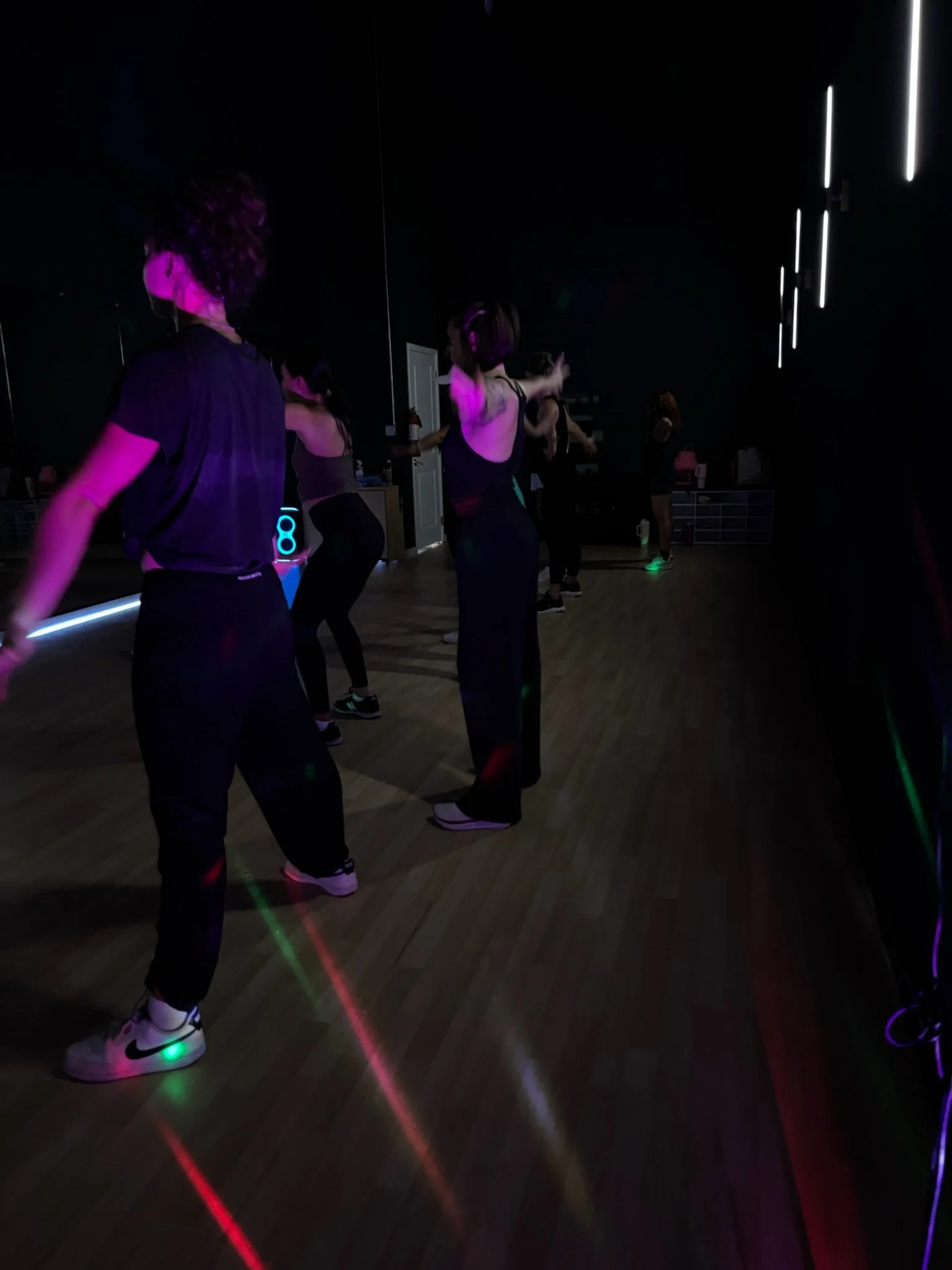 People participating in a dance fitness class in a dark room with neon lighting.