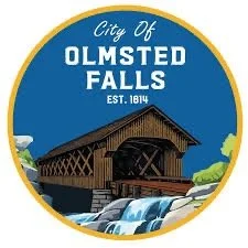 The emblem of Olmsted Falls featuring a covered bridge over a small waterfall with green hills in the background.