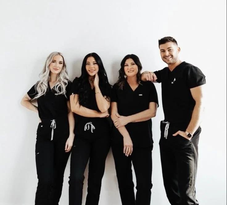 Four people wearing black scrubs standing against a white wall