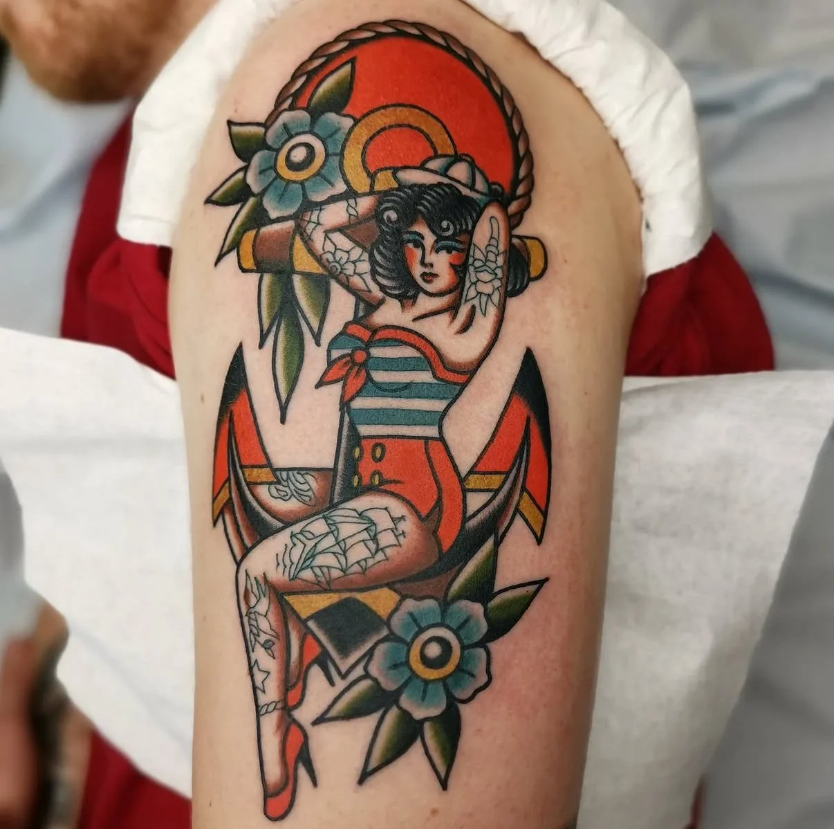 Tatouage d'une femme en style traditionnel, portant une tenue rayée avec un bandana rouge, entourée de fleurs et de feuilles, avec un design d'éléphant en arrière-plan.