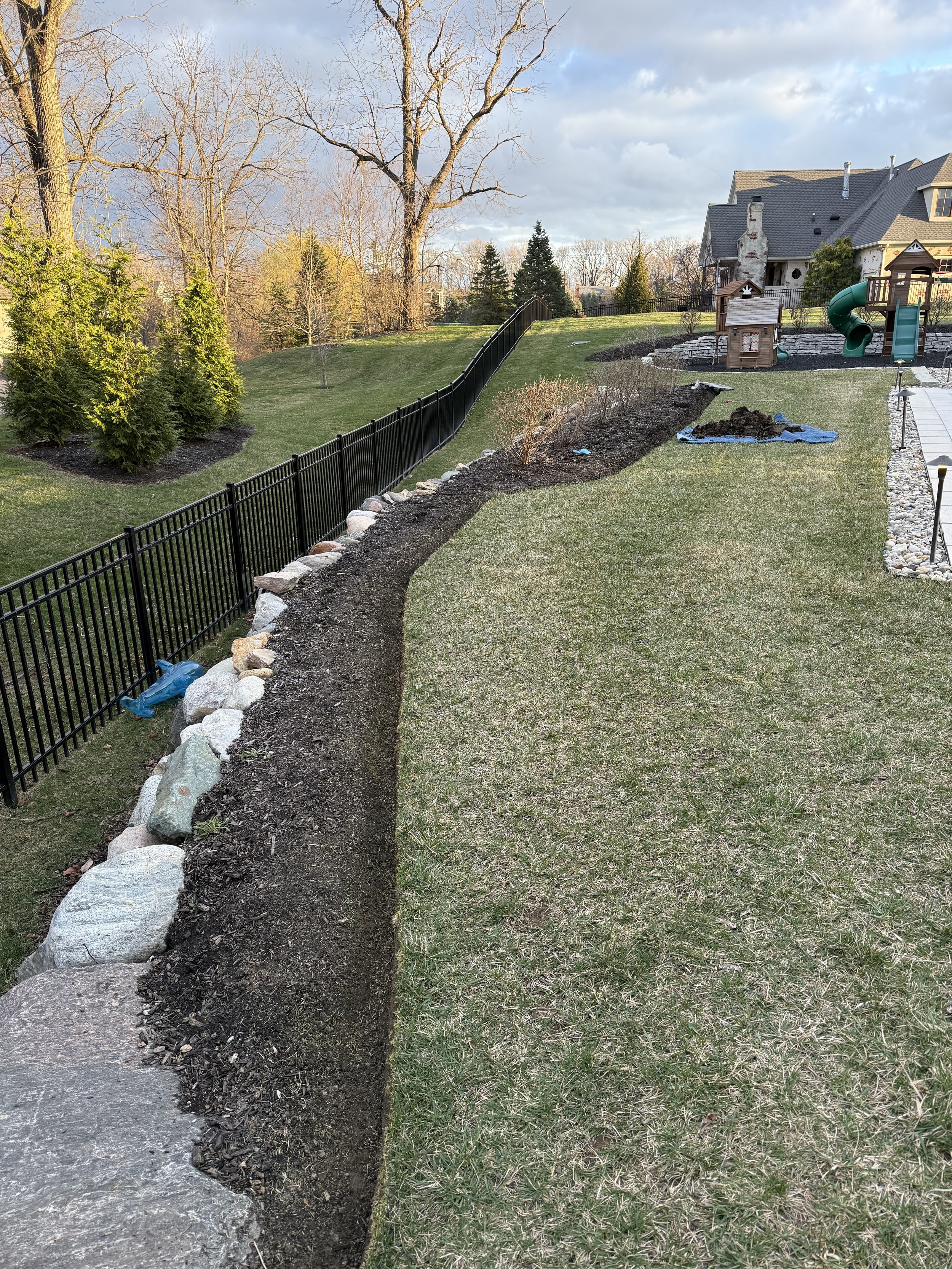 Newly landscaped backyard garden bed with crisp natural edging and black metal fence