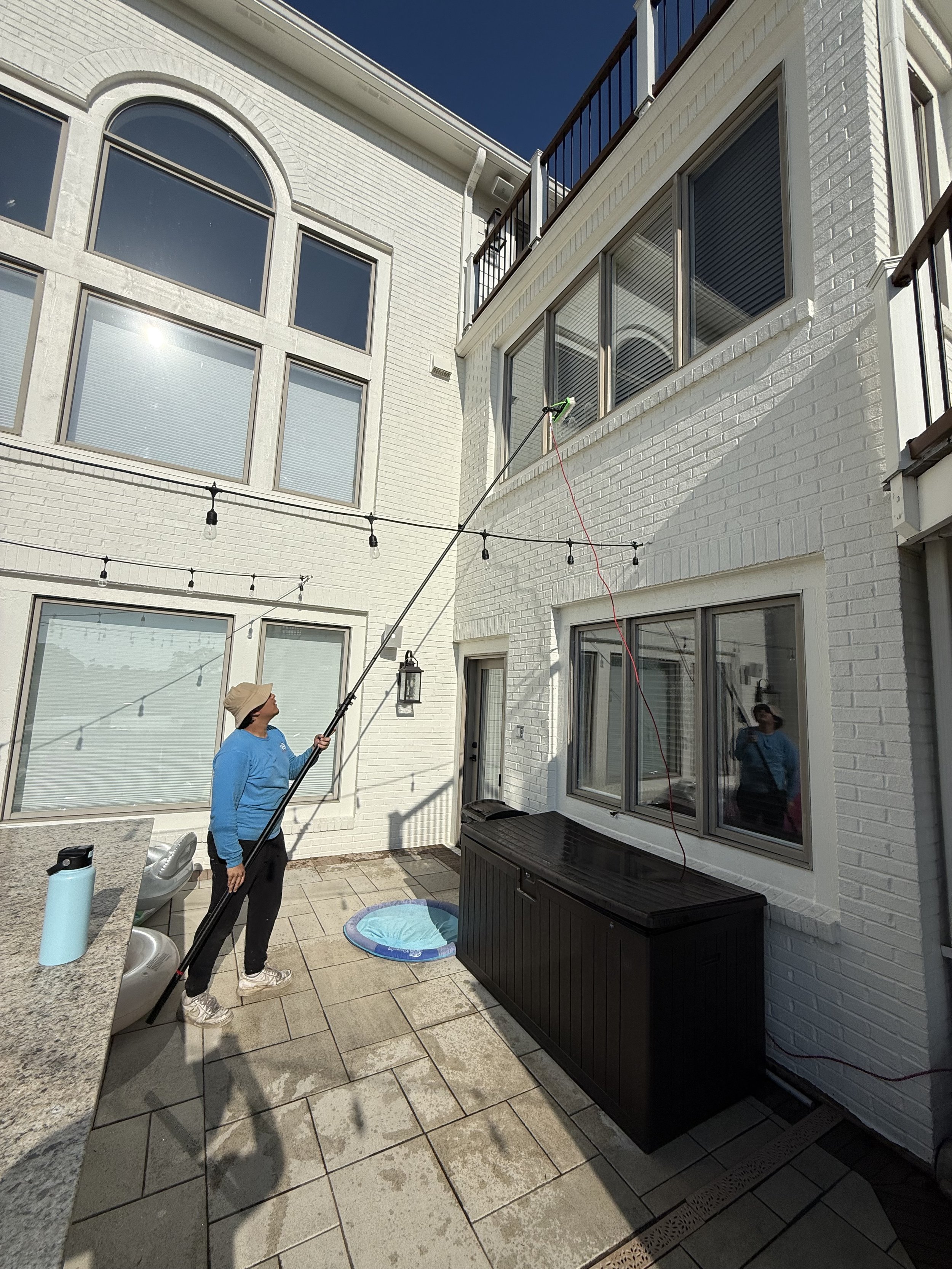 Residential second-story window cleaning using water-fed pole on white brick house in Noblesville
