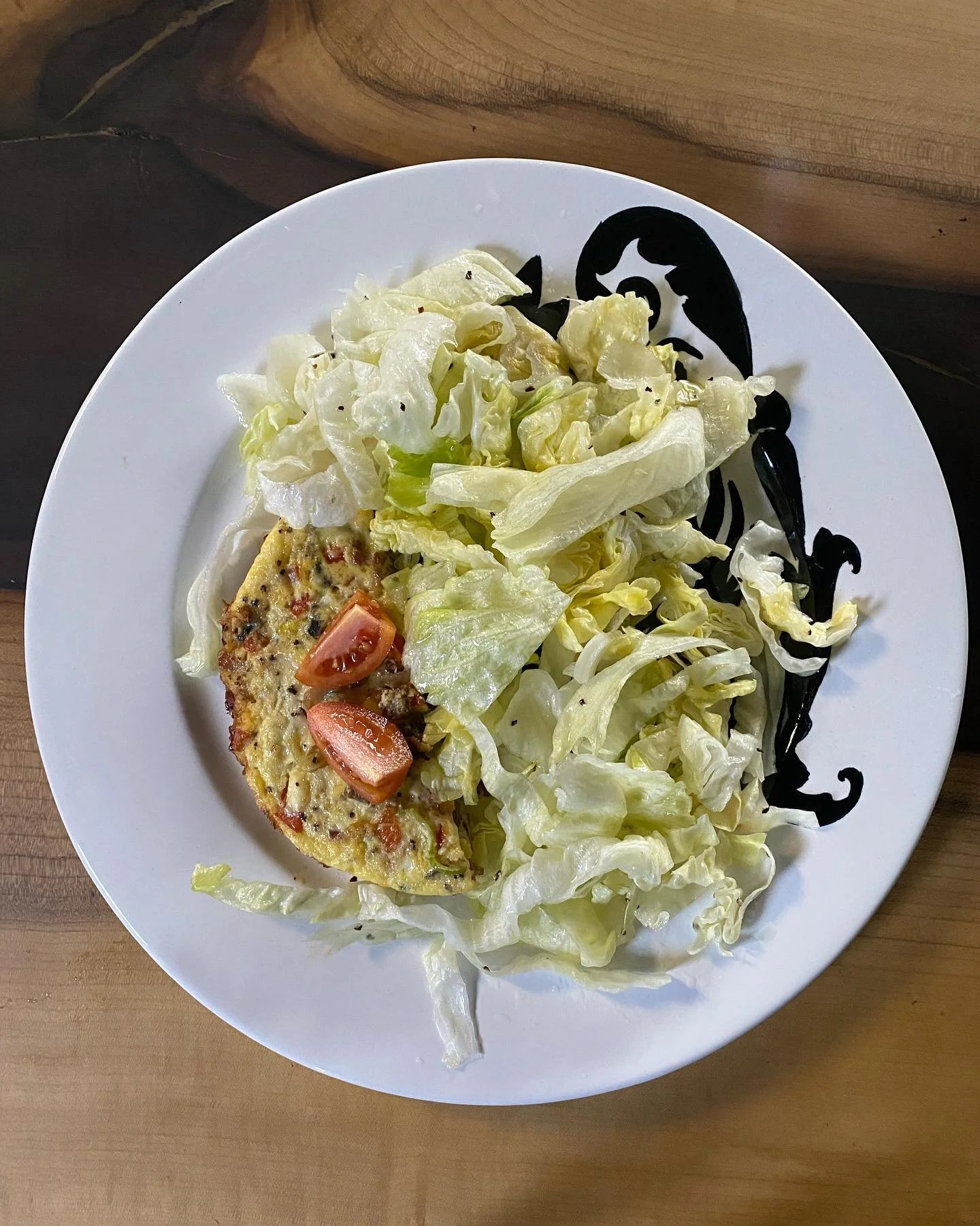 Plate with lettuce, cherry tomato, and a baked dish, on a wooden table.