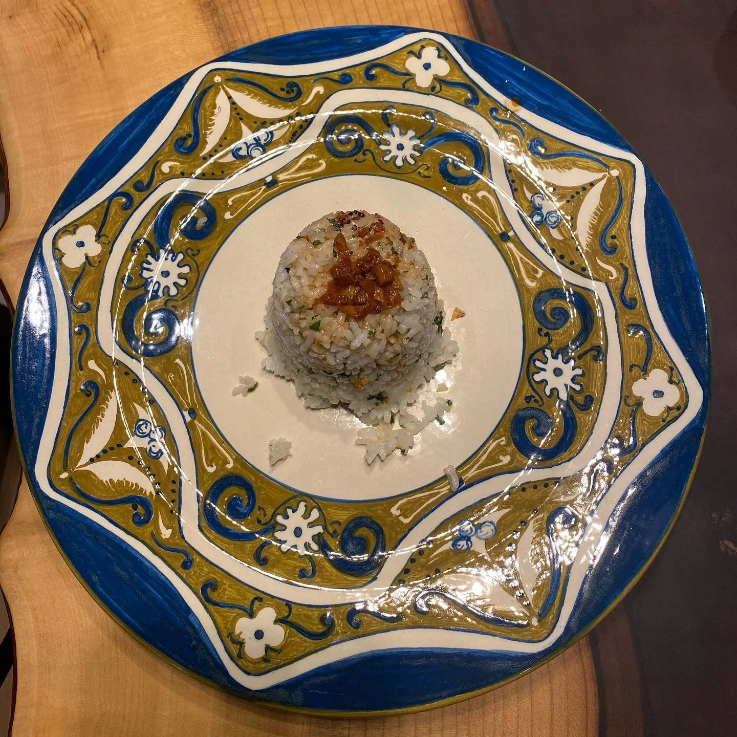 A plate with ornate blue, white, and gold patterns holding a serving of rice with a topping of cooked vegetables or meat.