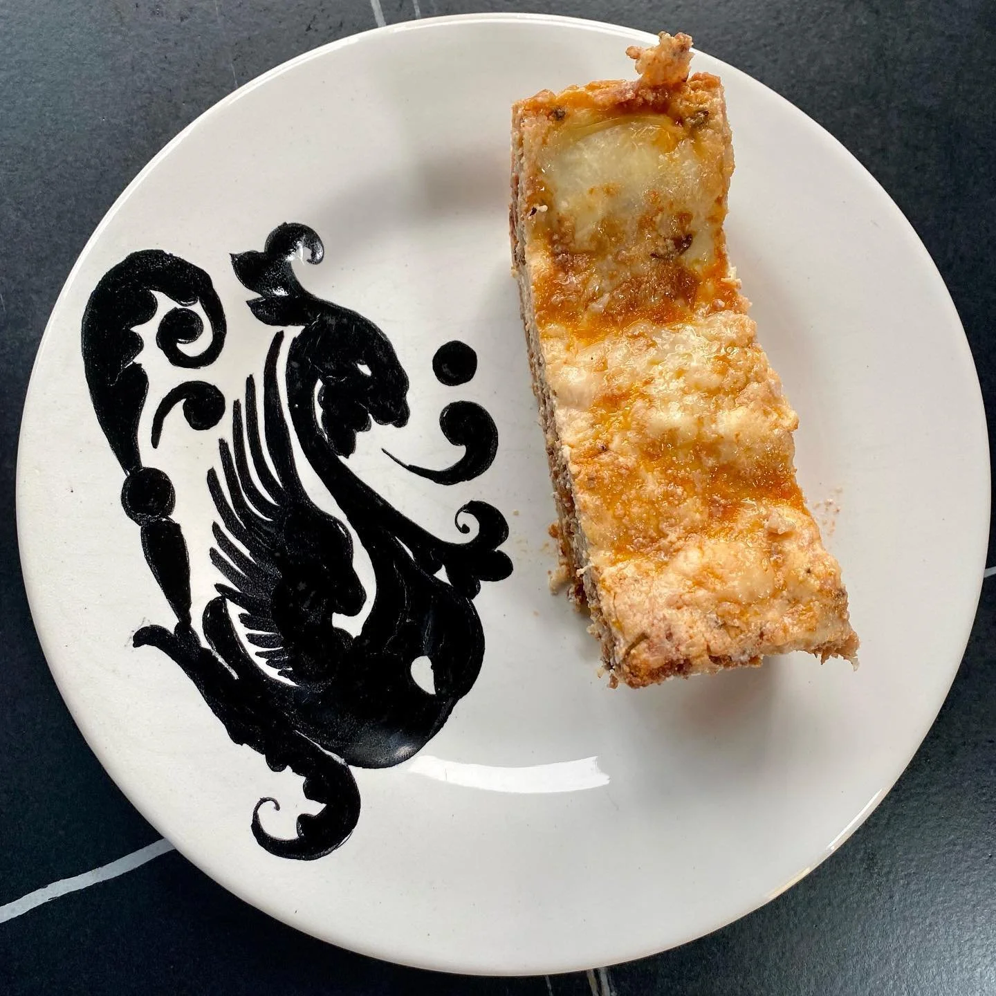 A slice of apple crumble pie on a white plate with a black lion design.