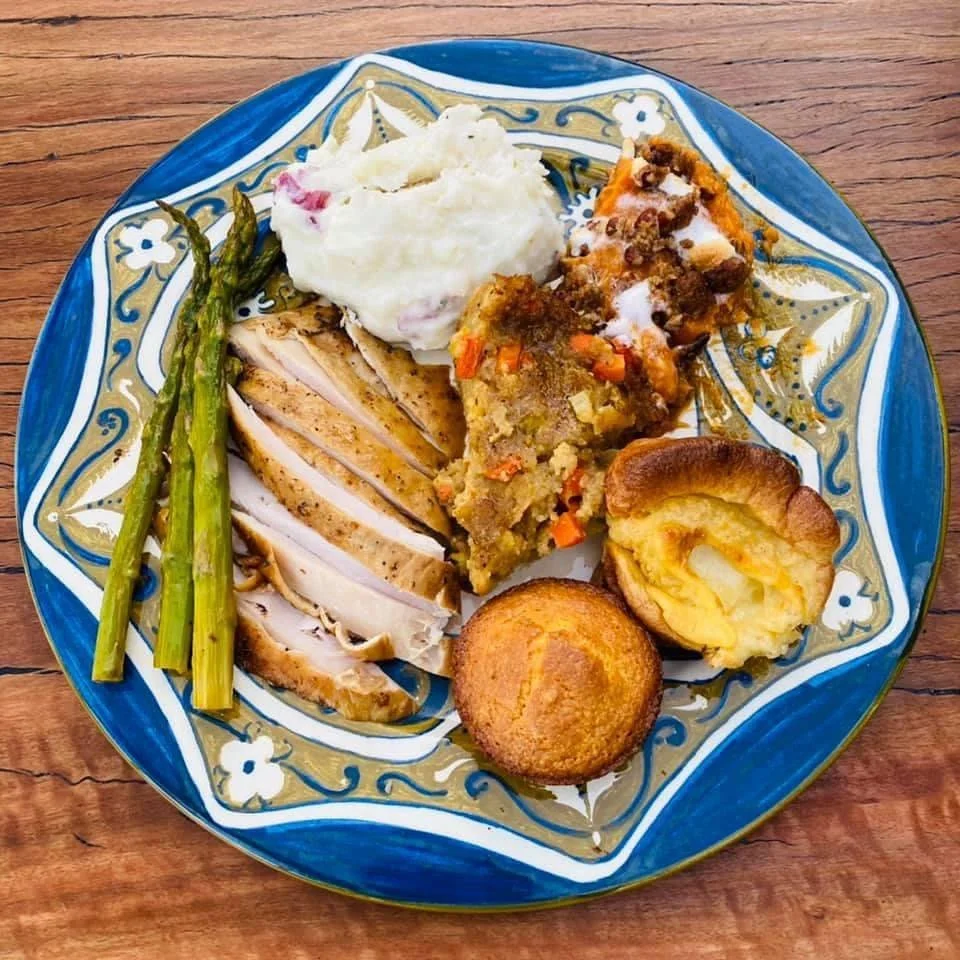 Plate with sliced turkey, roasted asparagus, mashed potatoes with gravy, vegetable casserole, Yorkshire pudding, and a cornbread muffin.