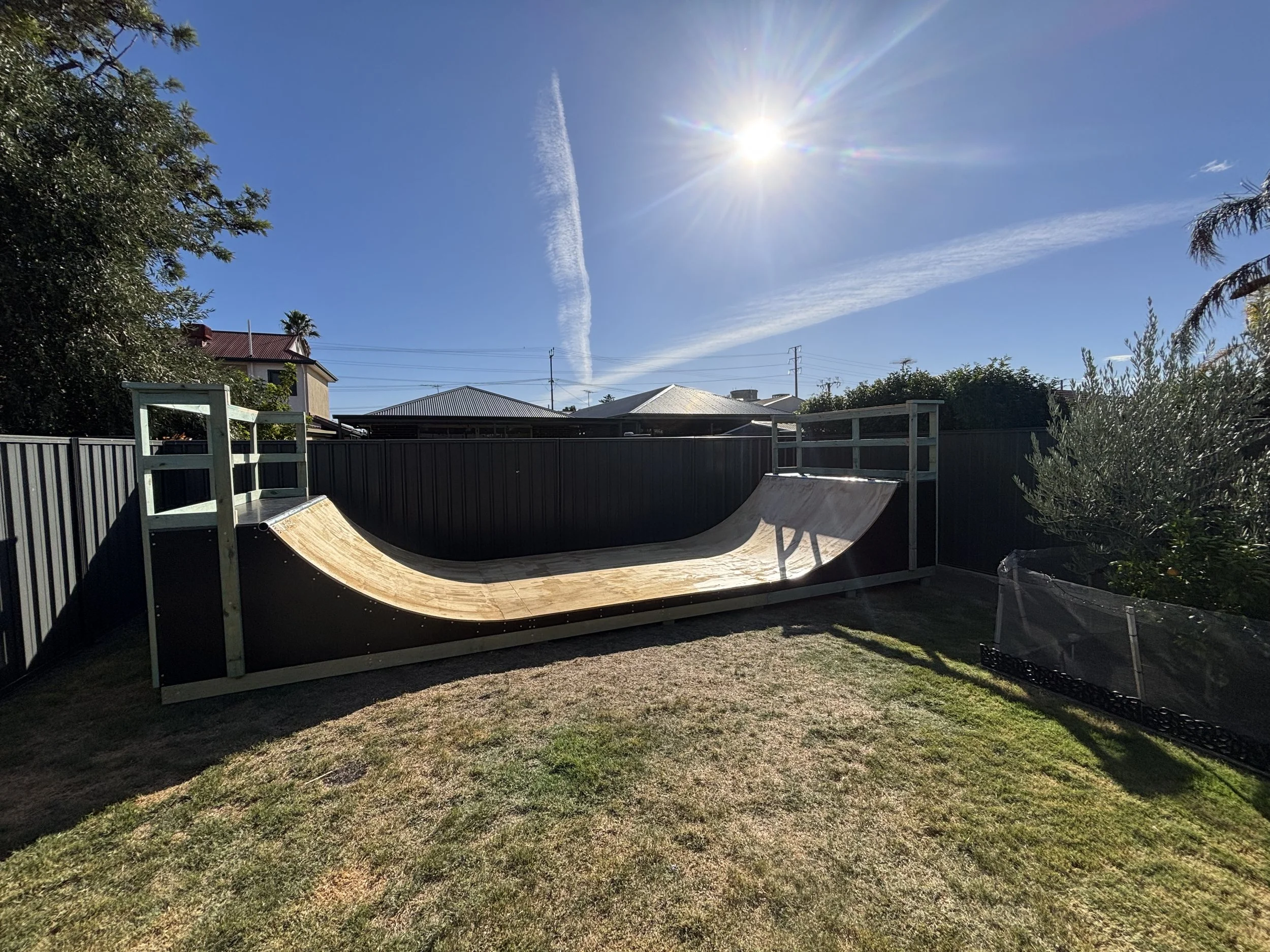 Backyard with a skateboard ramp under a clear blue sky and bright sun.