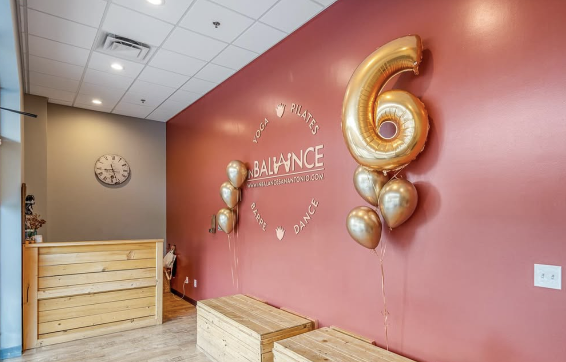 Yoga and Pilates studio with red wall, reception desk, a large number six balloon, and smaller gold balloons.