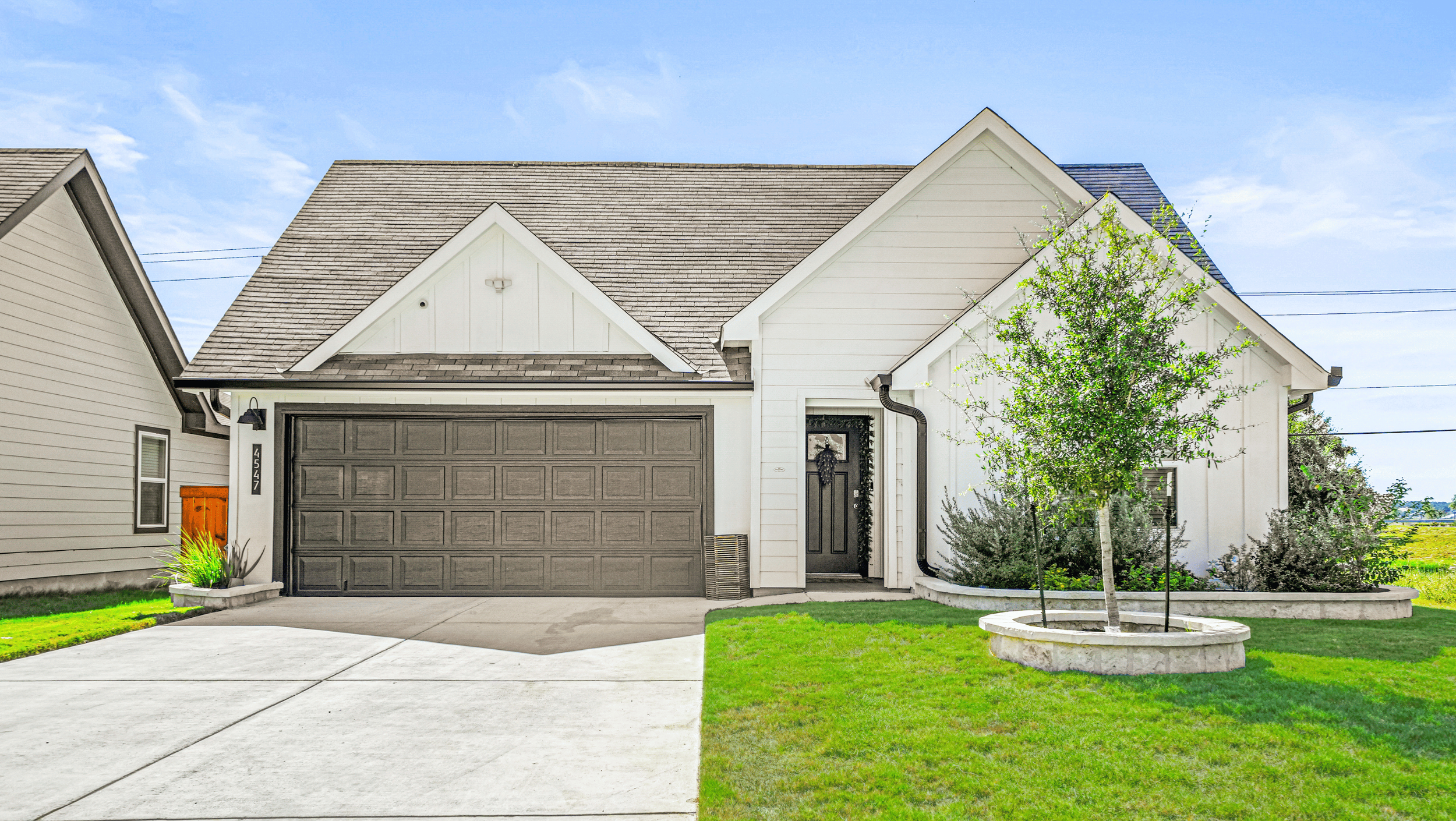 Modern single-story house with a double garage, front yard, and tree, under a clear blue sky.