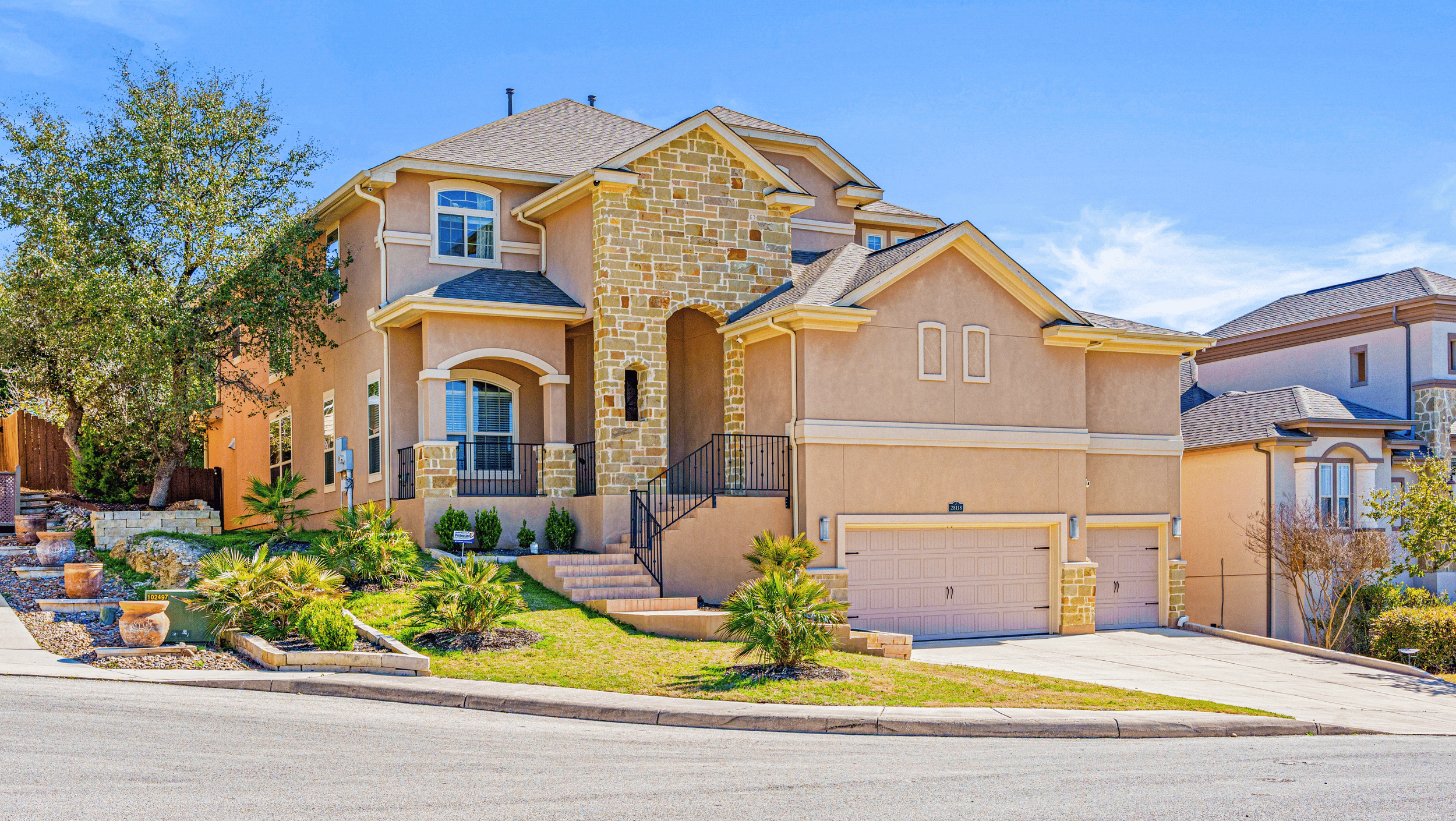 Two-story suburban house with stone and stucco exterior, three-car garage, front steps, and landscaped yard.