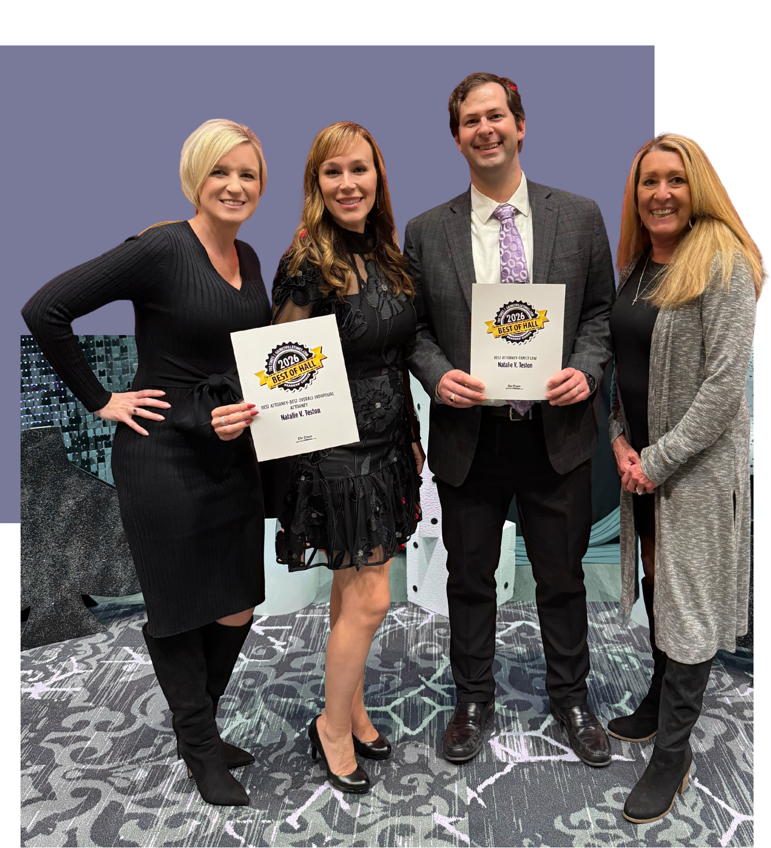 Four people attending an awards ceremony, two women holding certificates, and a man standing between them, all smiling and dressed formally, with a purple background.