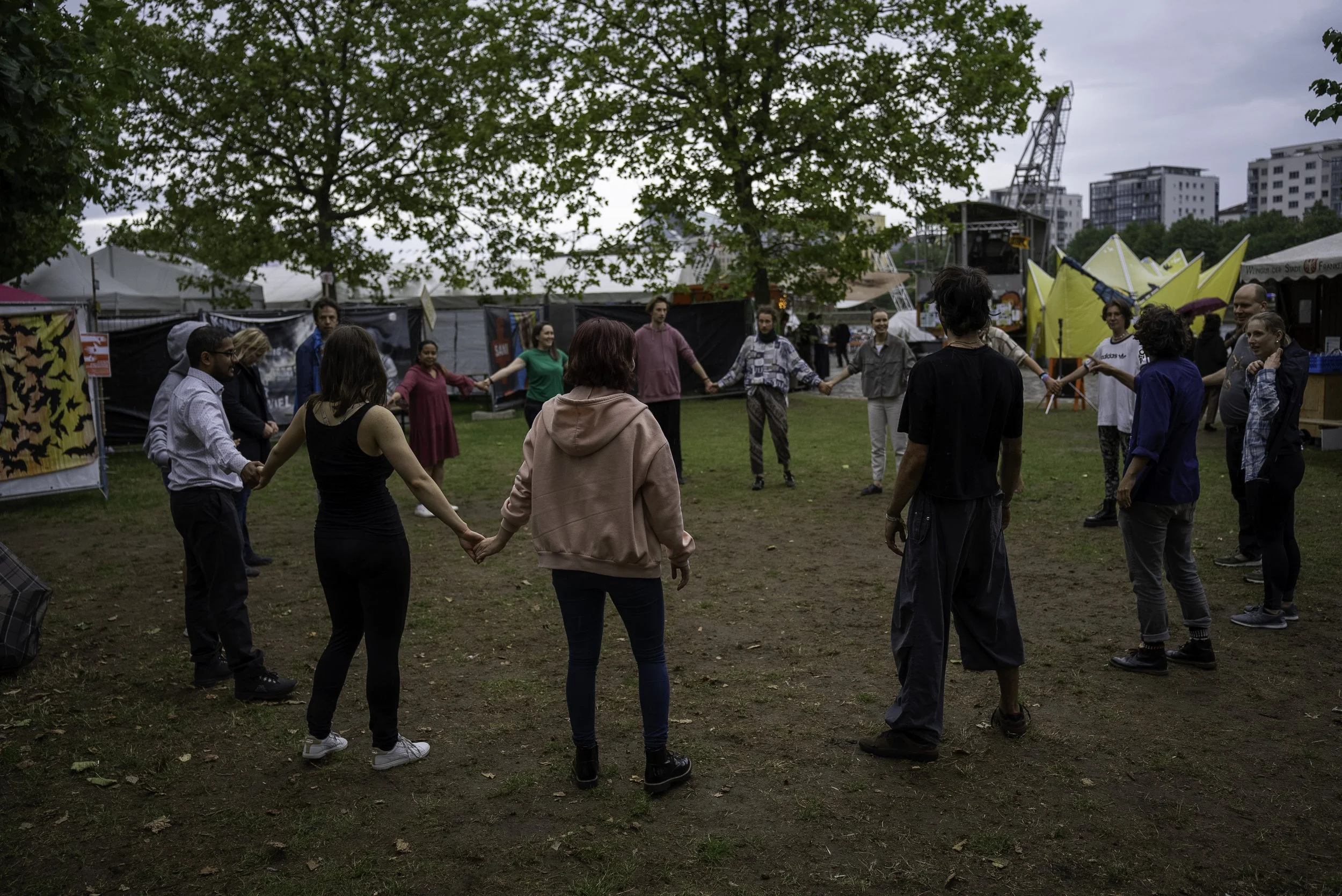 People holding hands in a circle outdoors during daytime at a festival or event.