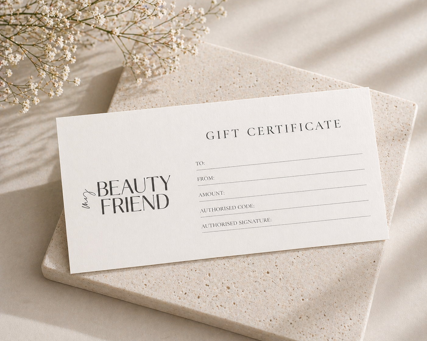 A gift certificate labeled 'Beauty and Friend' resting on a textured light-colored surface, with a sprig of white flowers nearby.