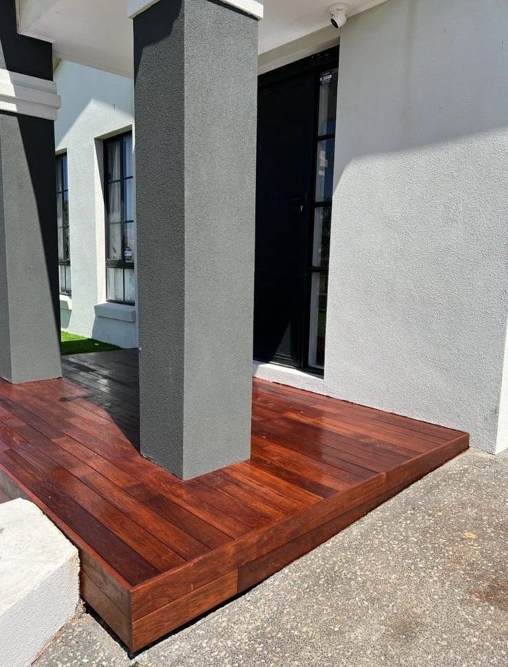 Exterior view of a house with a small wooden porch, grey columns, white walls, and a black door.