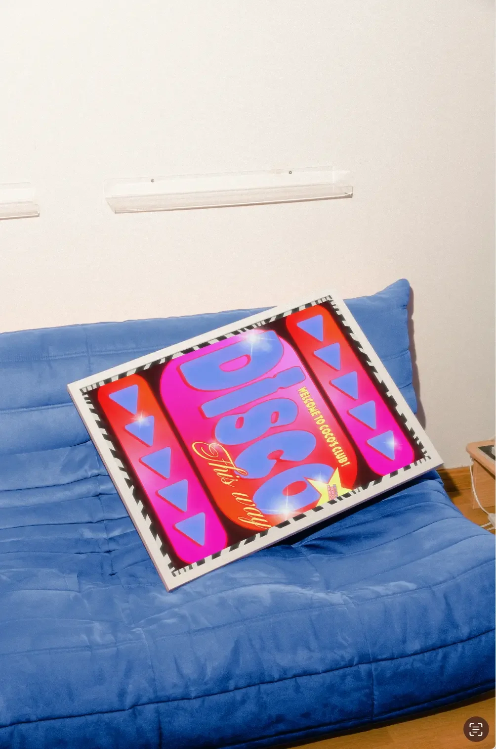 Un tableau coloré avec le mot 'WOW' en gros caractères, posé sur un canapé bleu, dans une pièce avec un mur blanc.