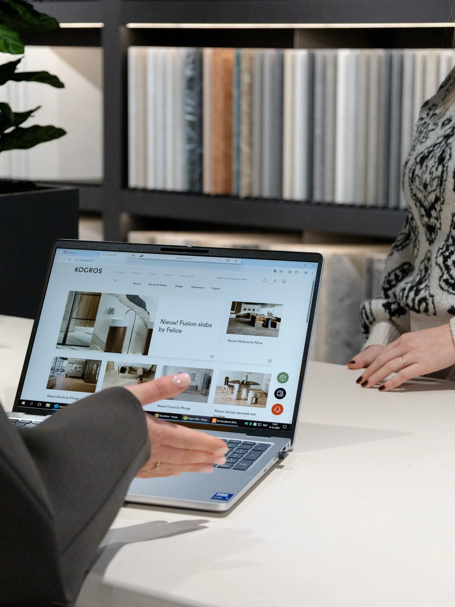 Een persoon wijst naar een laptop met een website voor b2b, terwijl een andere persoon ernaast kijkt.