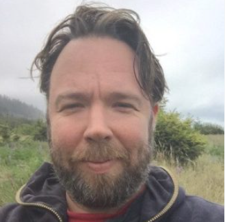 Bearded man smiling in front of a pastoral green background