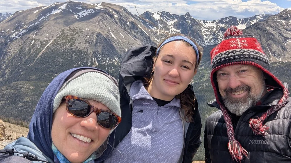 3 people in a selfie with a rocky mountain backdrop