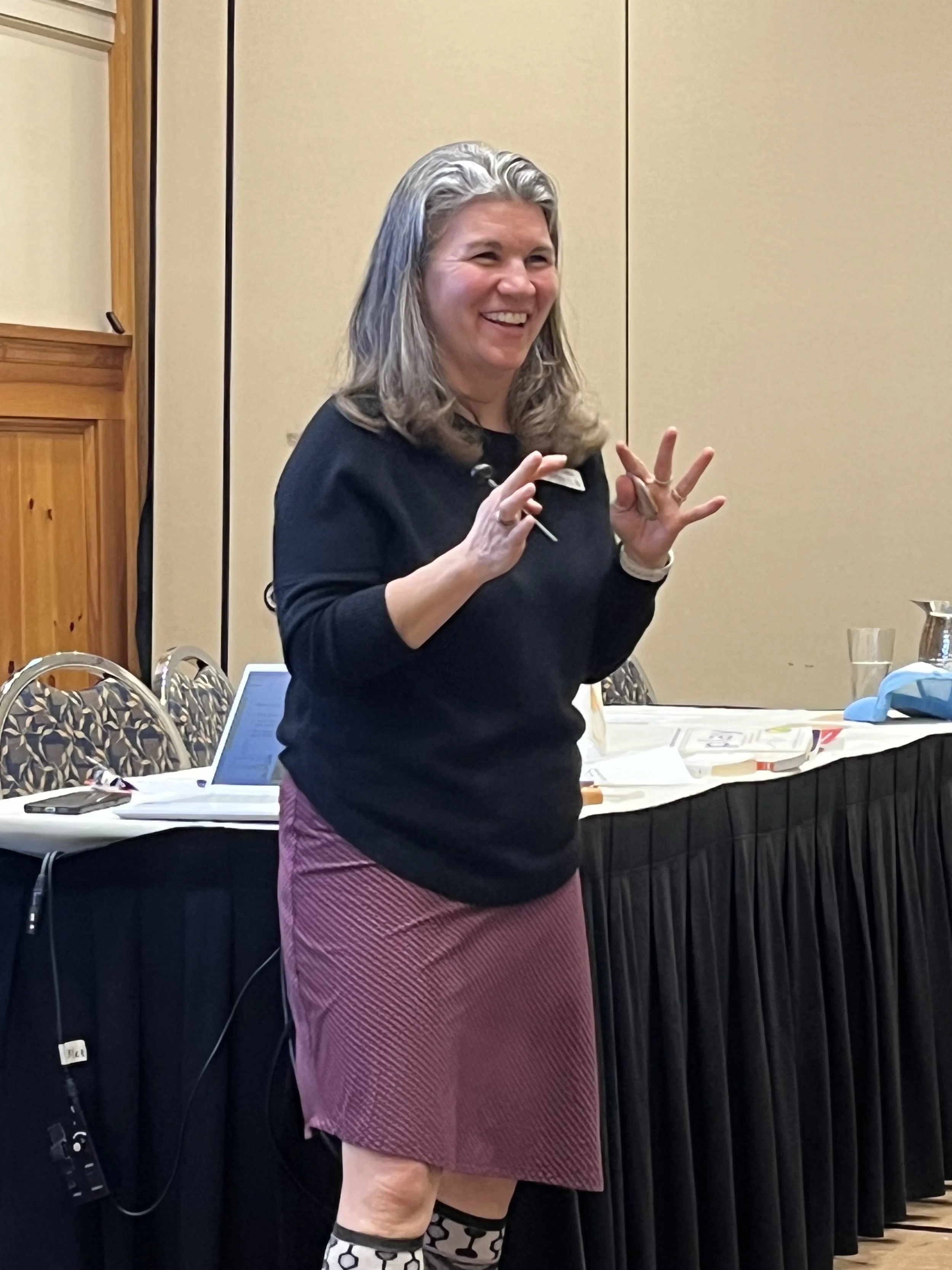 woman smiling, in a black sweater and striped skirt