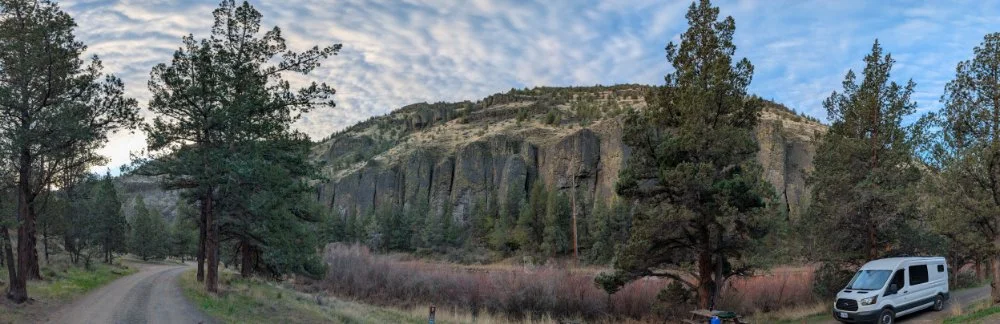 panoramic image of the Crooked River canyon with pine trees and a cloudy blue sky