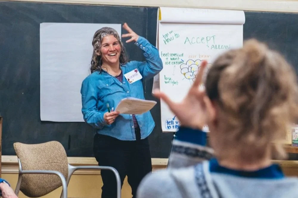 Female facilitatar in blue laughing while making hand motion with participant