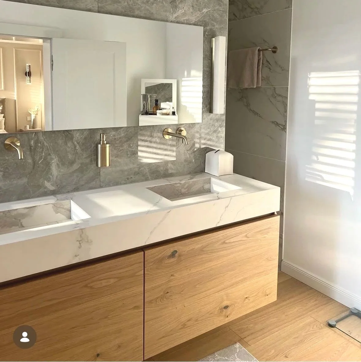 Moderner Badezimmerwaschbereich mit zwei Waschbecken, Holzschrank und großen Spiegel. Beleuchtung und Handtuchhalter sind sichtbar.