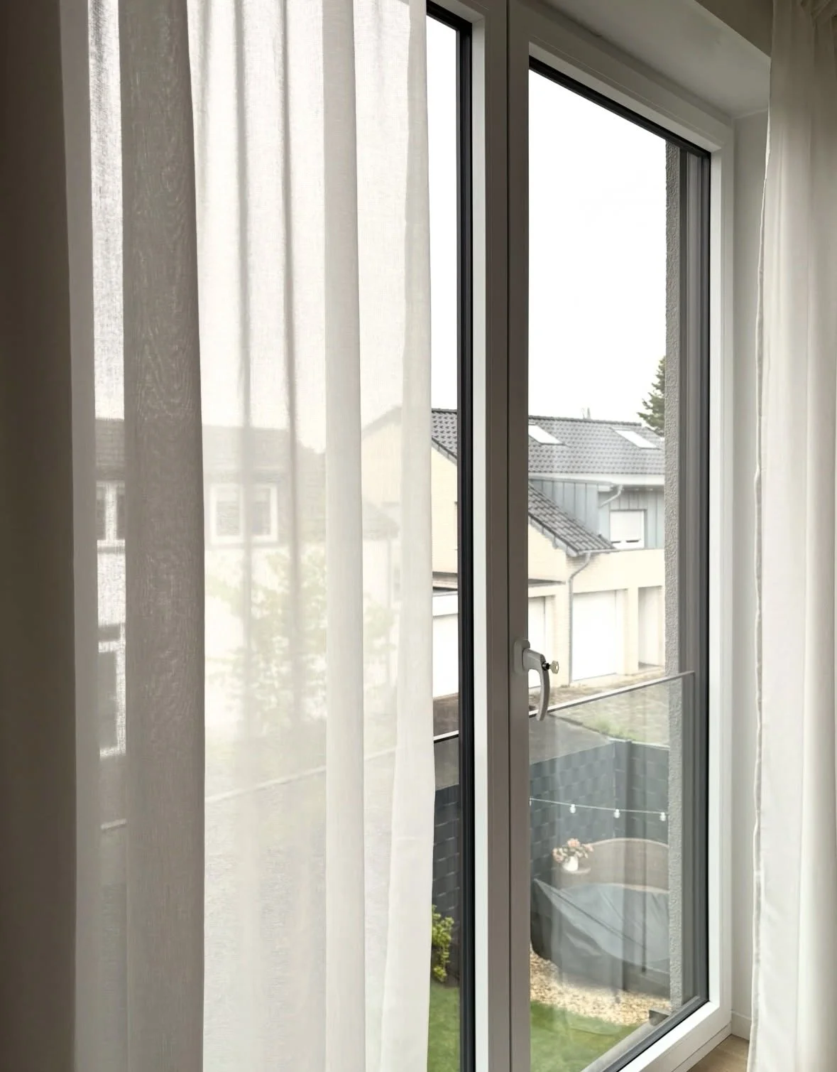 Fenster mit weißen Vorhängen, Blick nach draußen auf Nachbarhäuser und Garten, mit Balkon