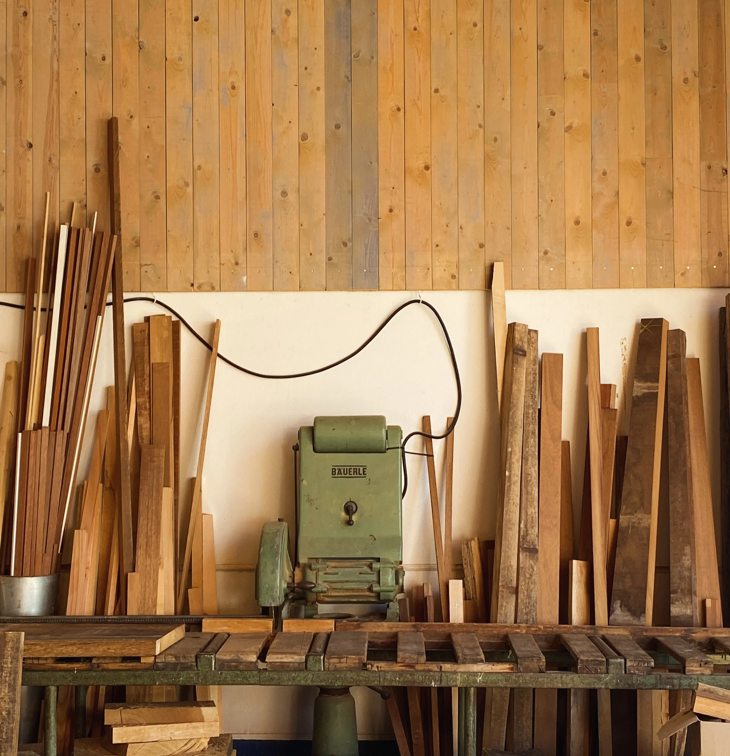 Holzwerkstatt mit Holzstapeln, Handwerksmaschinen und Werkbänken, Wand aus Holzpaneelen.