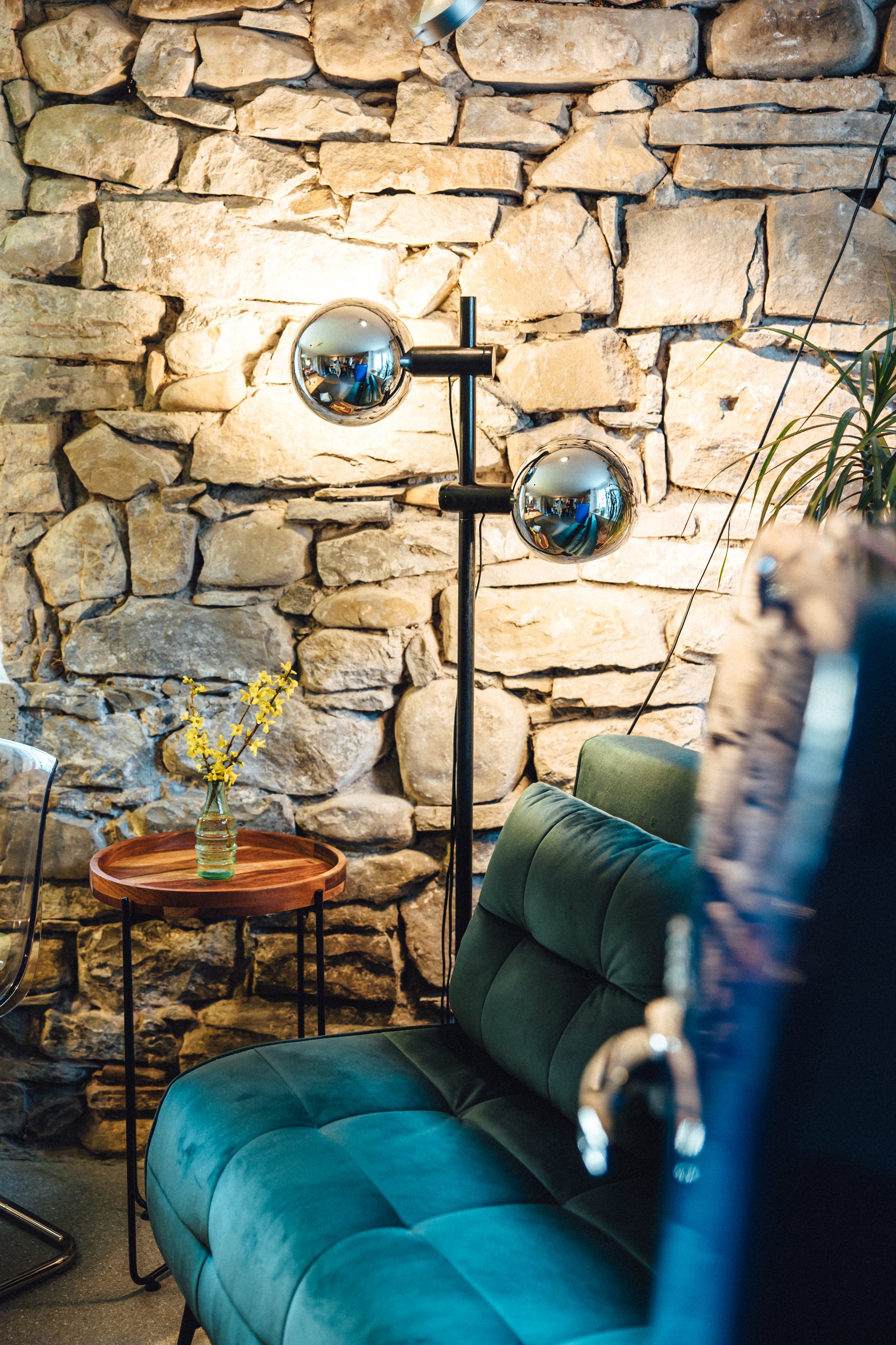 Steinmauer beleuchtet von Retro-Stehlampe, Schlafsofa mit Beistelltisch und Blumendeko